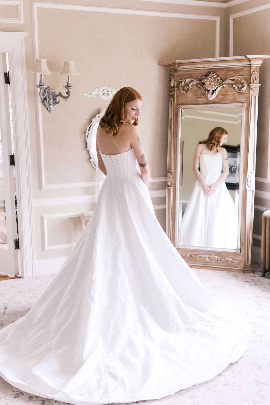 Bride in a strapless wedding gown standing beside an ornate mirror during bridal portraits at Longview Mansion
