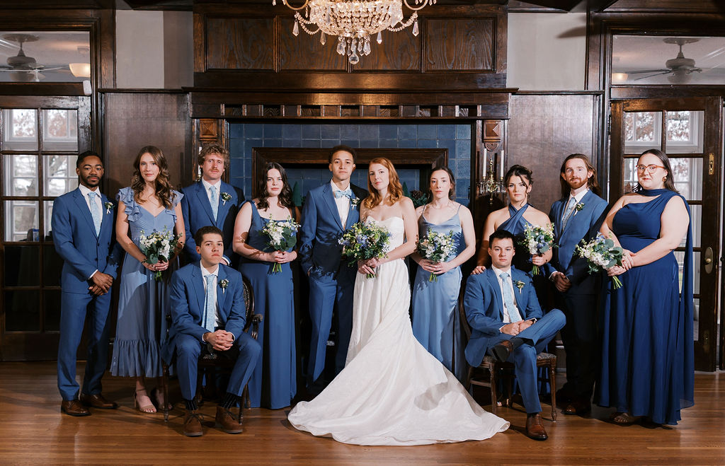 Wedding party portrait with bride, groom, bridesmaids, and groomsmen in front of a grand fireplace at Longview Mansion.
