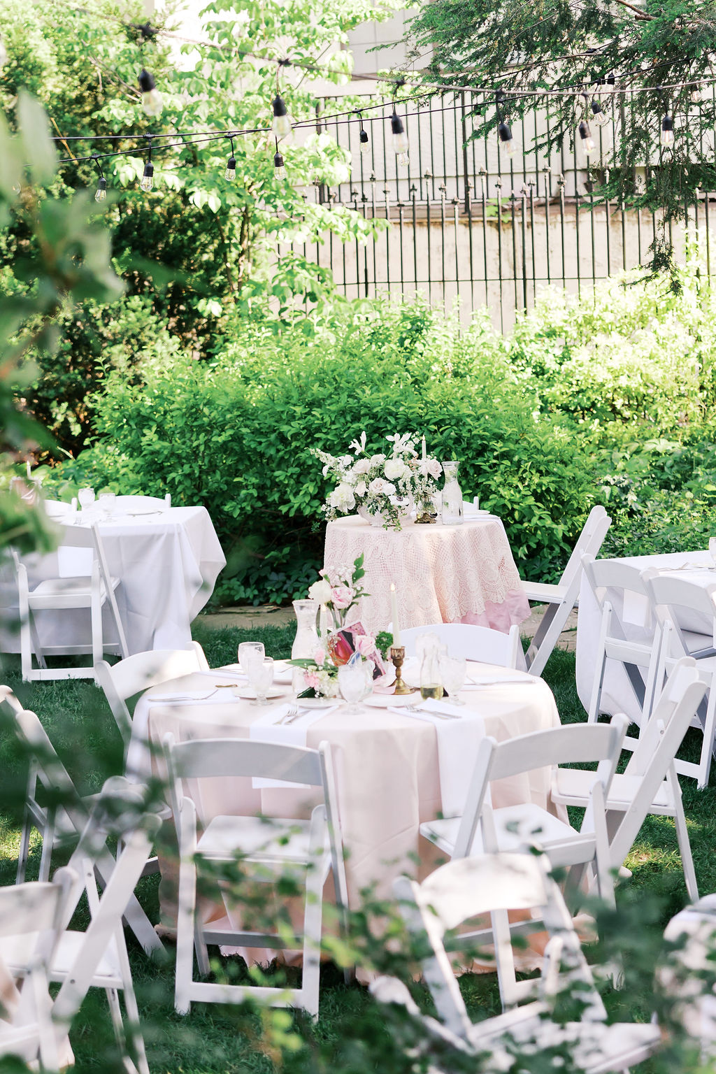 Outdoor wedding reception tables with white linens and floral centerpieces beneath string lights at Simpson House