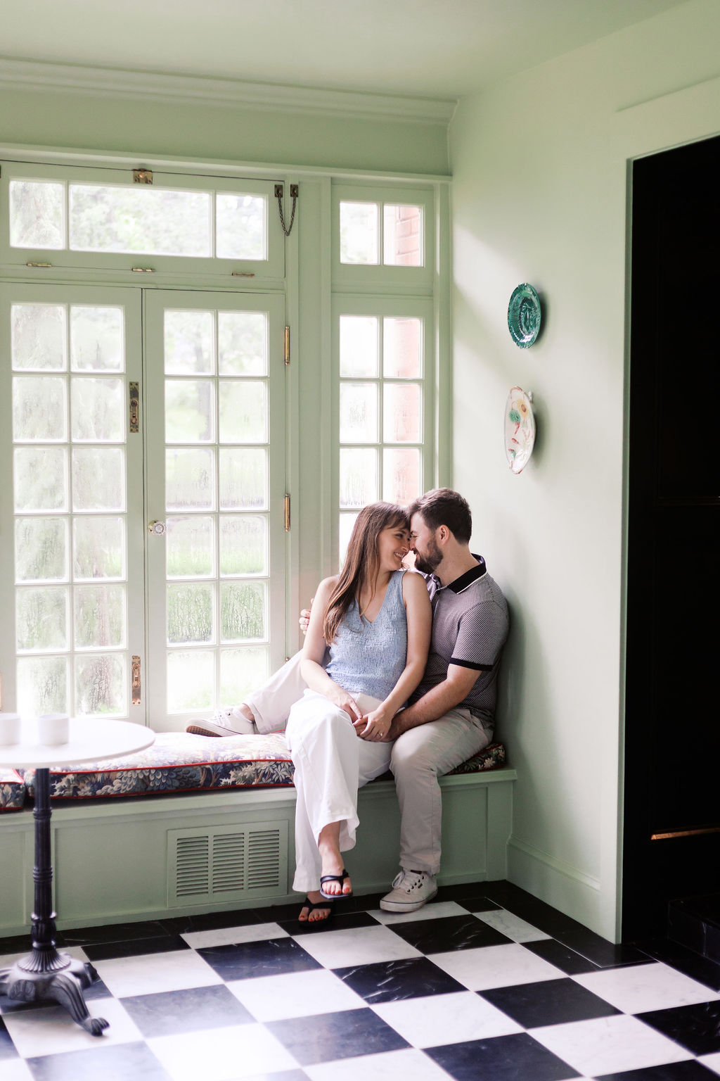 Engaged couple cuddling on a window seat inside a bright historic home during their engagement session at The Truitt
