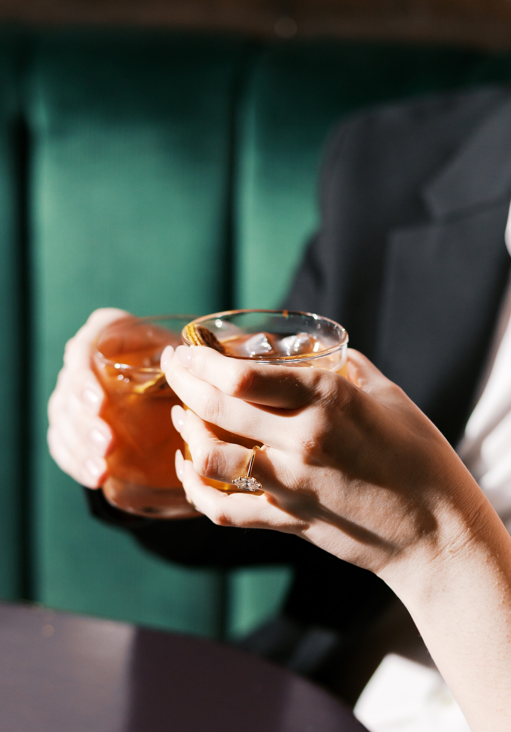 Close-up of an oval engagement ring as the couple holds old fashioned cocktails.