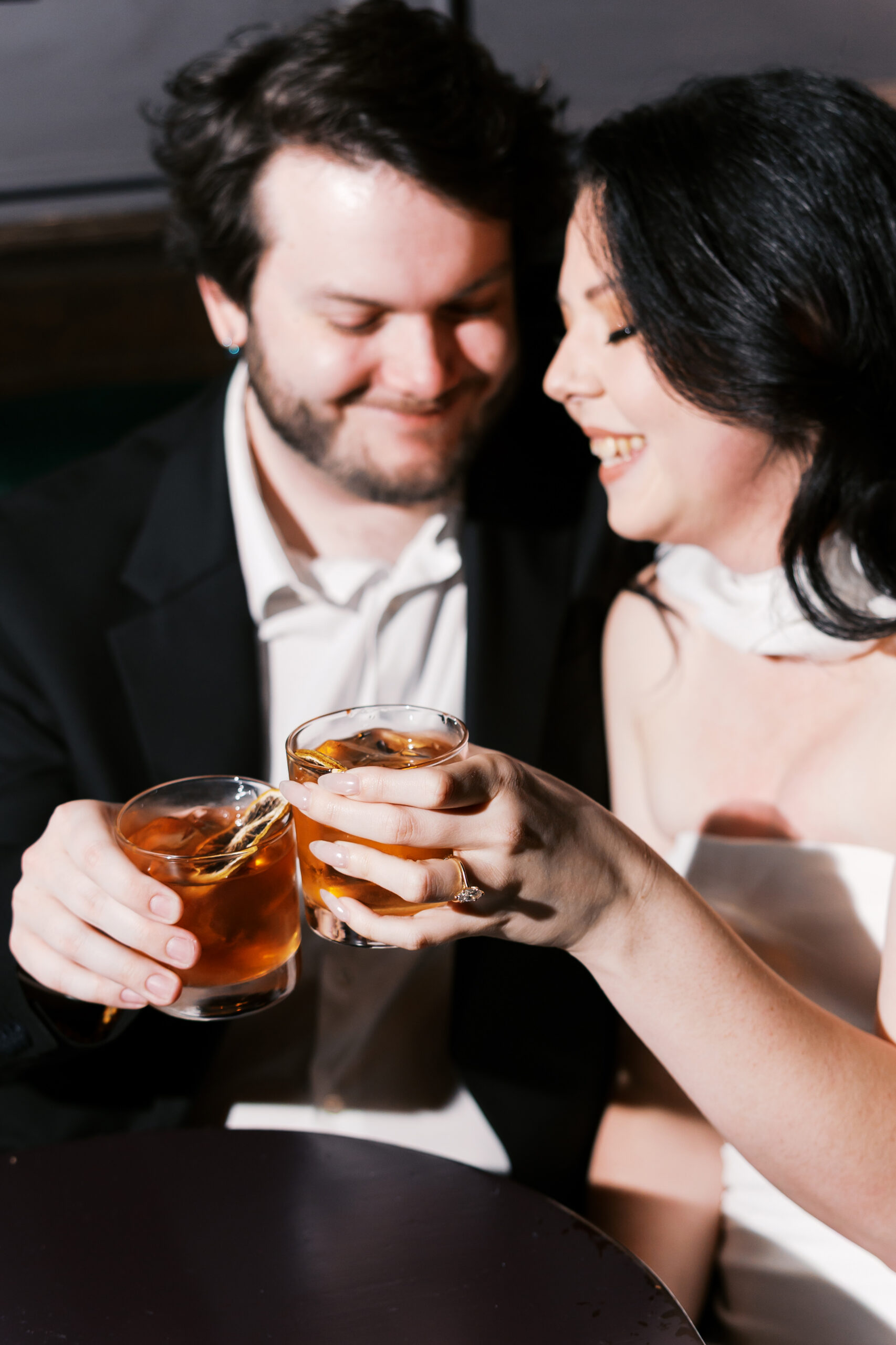 Couple toasting with cocktails during an engagement session, with the engagement ring in focus.