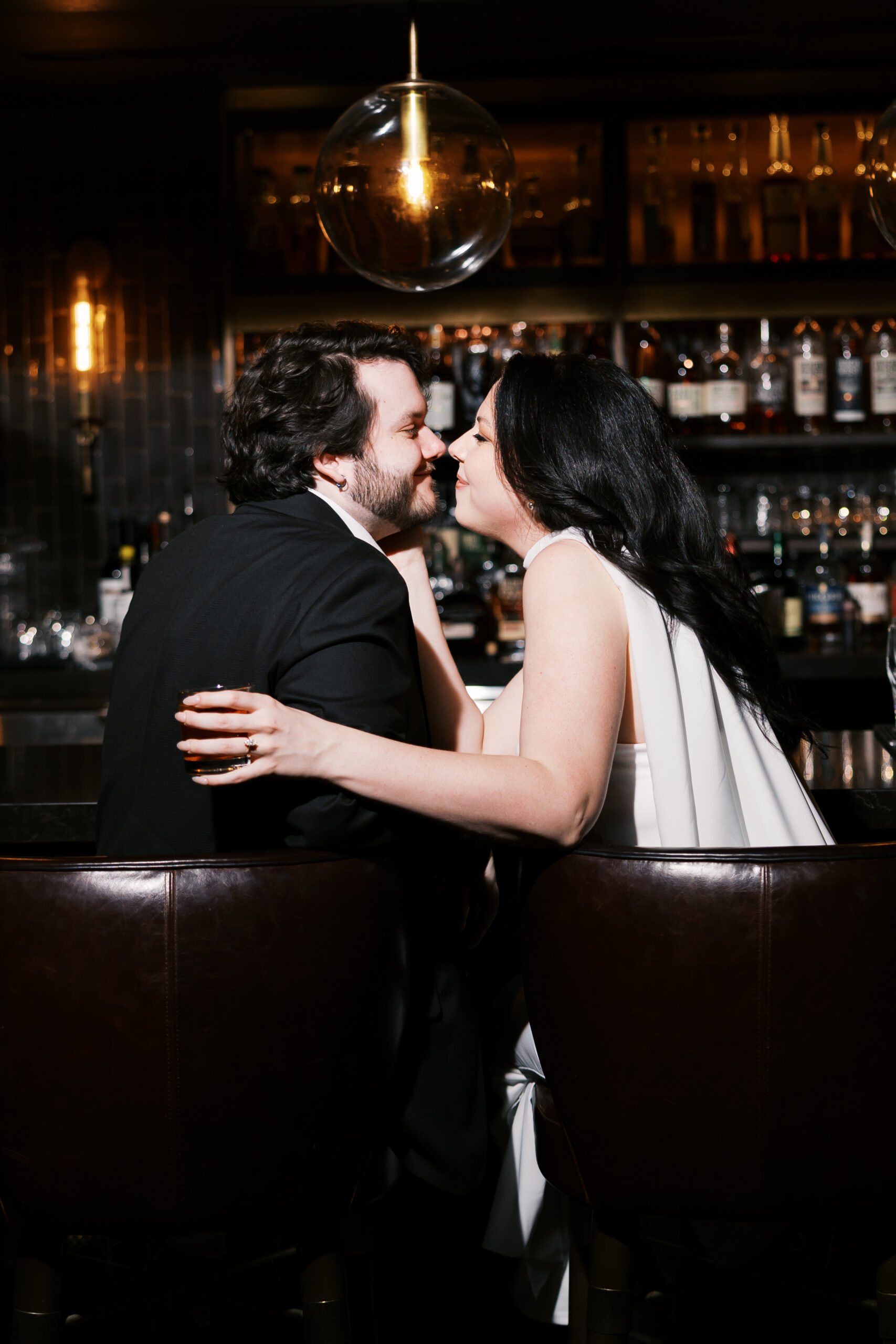 Couple leaning in for a kiss while seated at the bar, surrounded by warm pendant lighting.