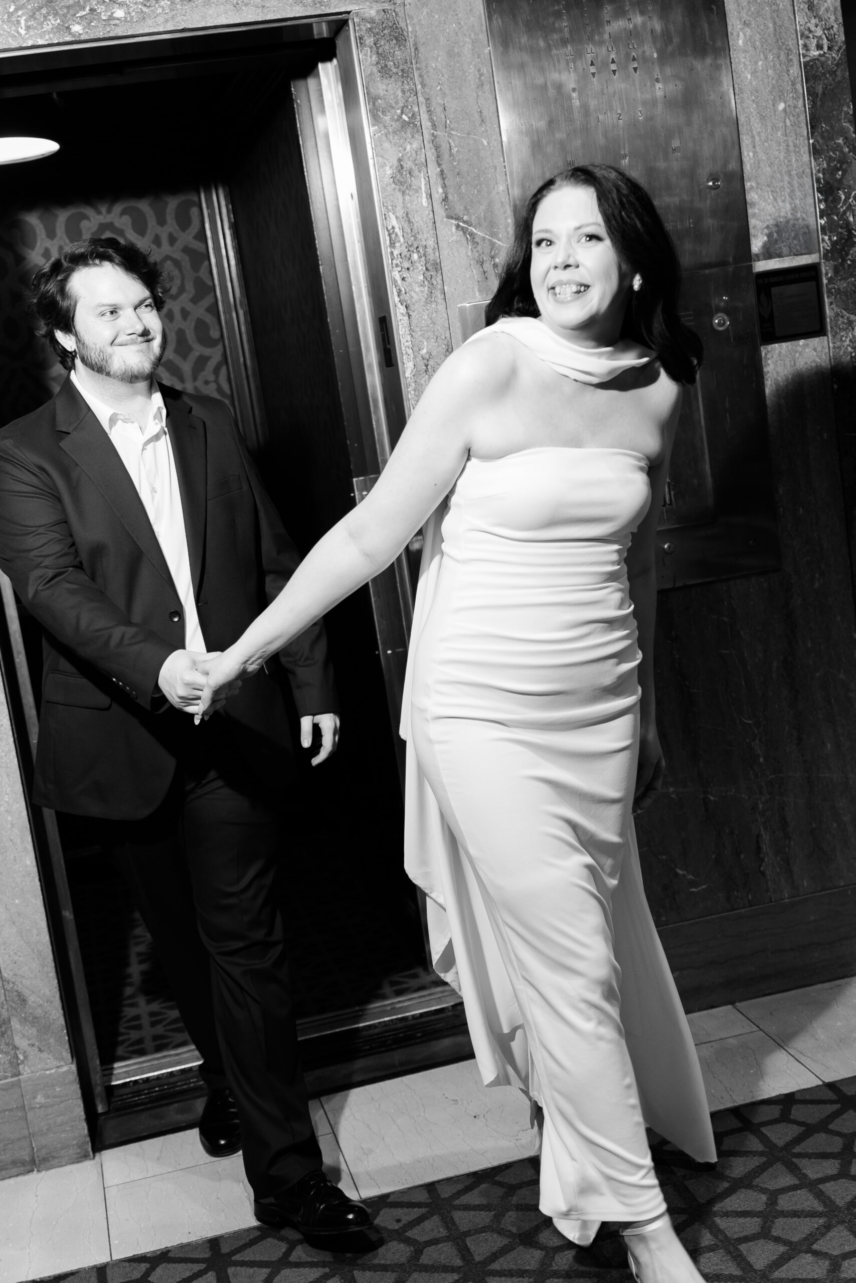 Black-and-white photo of the couple walking hand in hand from the hotel elevator.