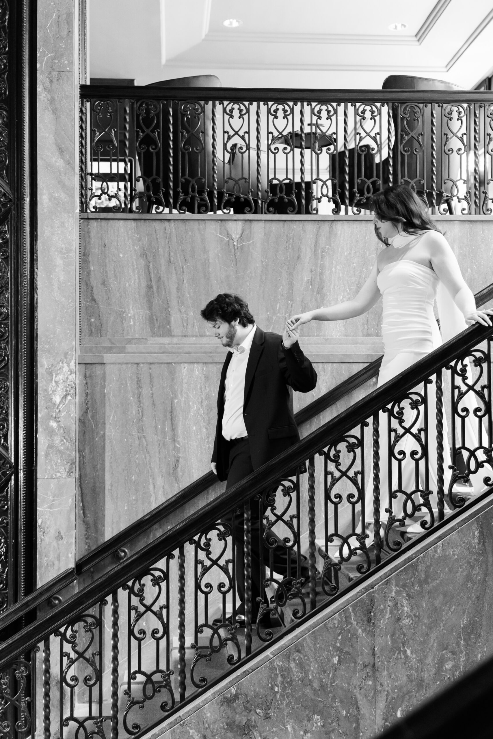 Black-and-white photo of the couple holding hands while walking down the hotel's marble staircase.