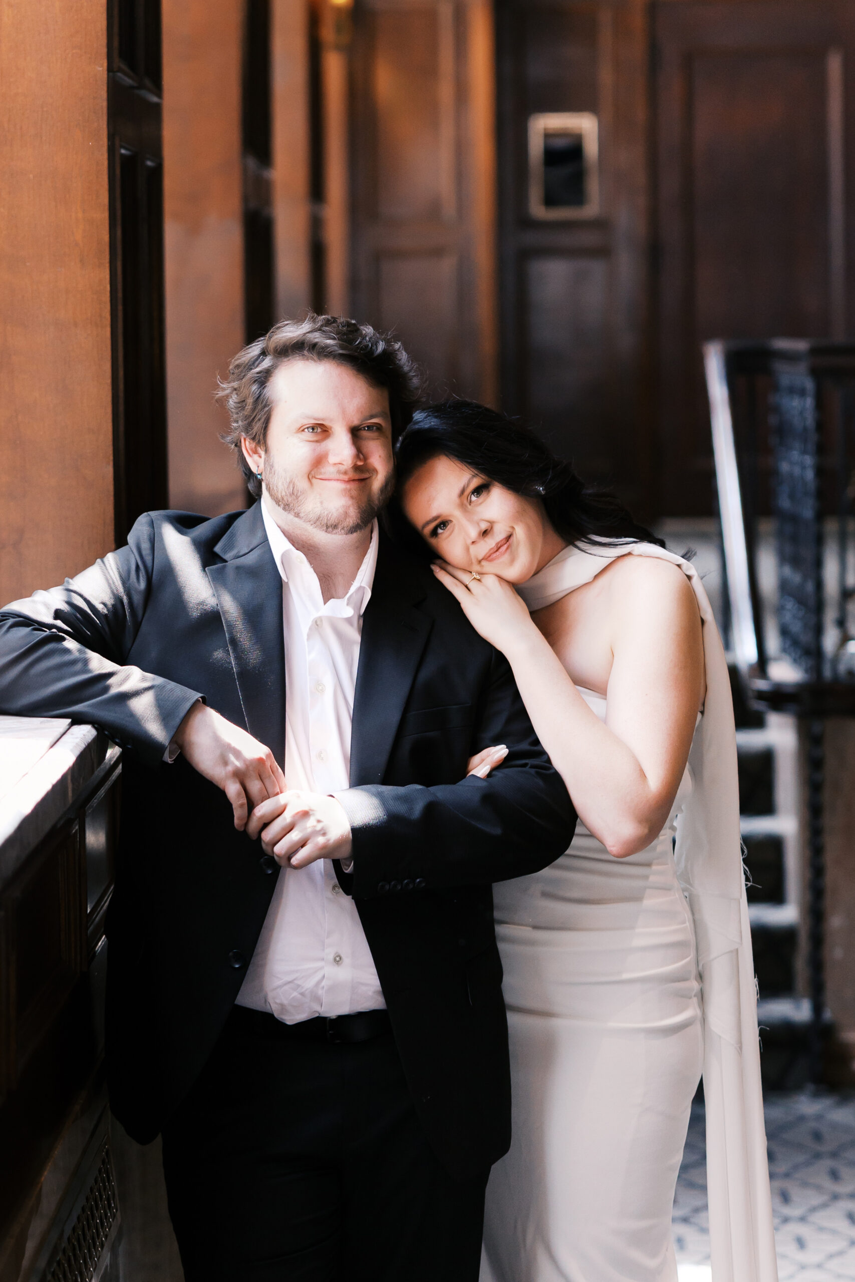 Couple leaning together by a sunlit window during their engagement session.