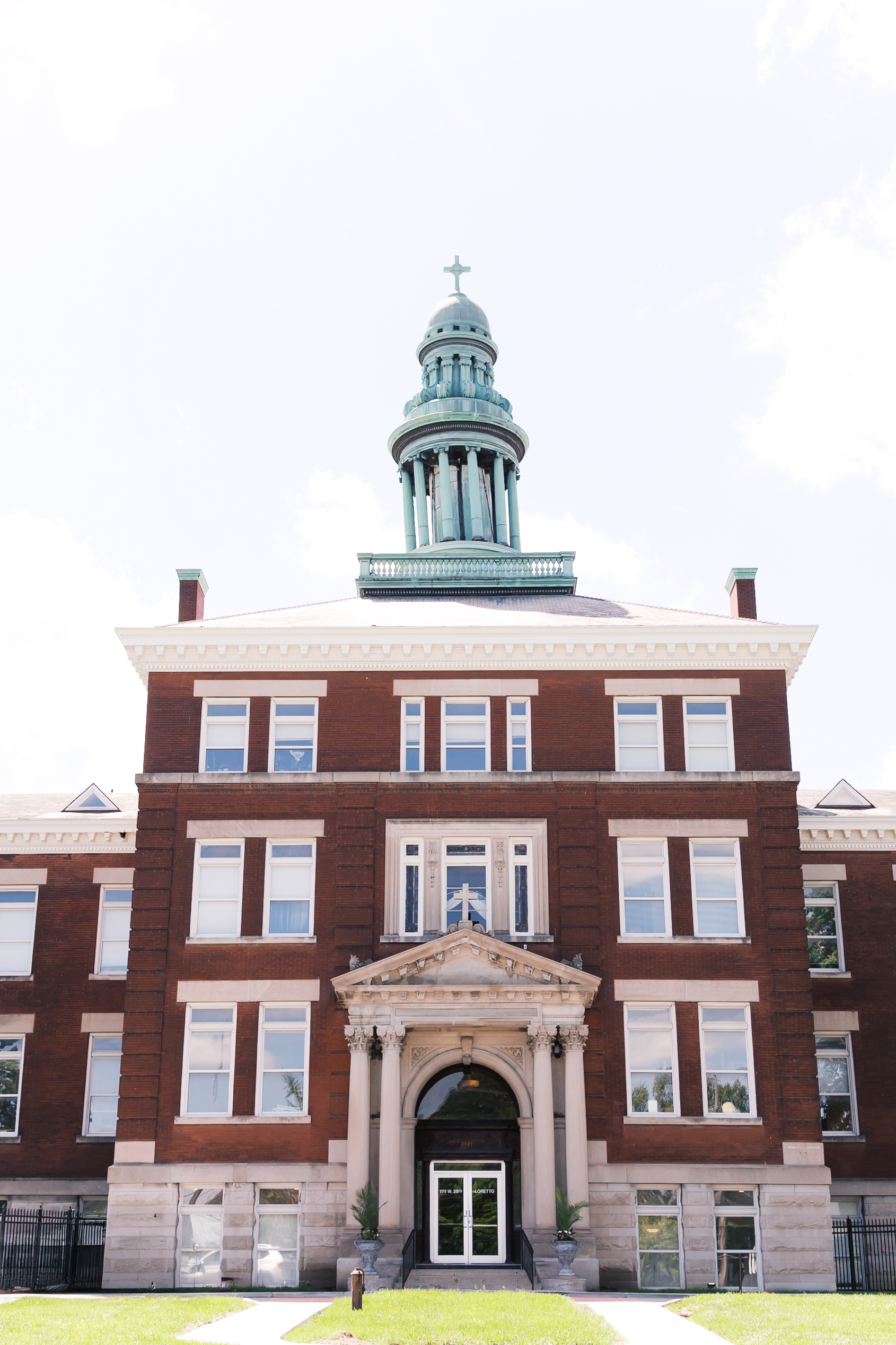 Historic brick exterior of The Loretto wedding venue with its iconic copper dome and grand front entrance under a bright blue sky.