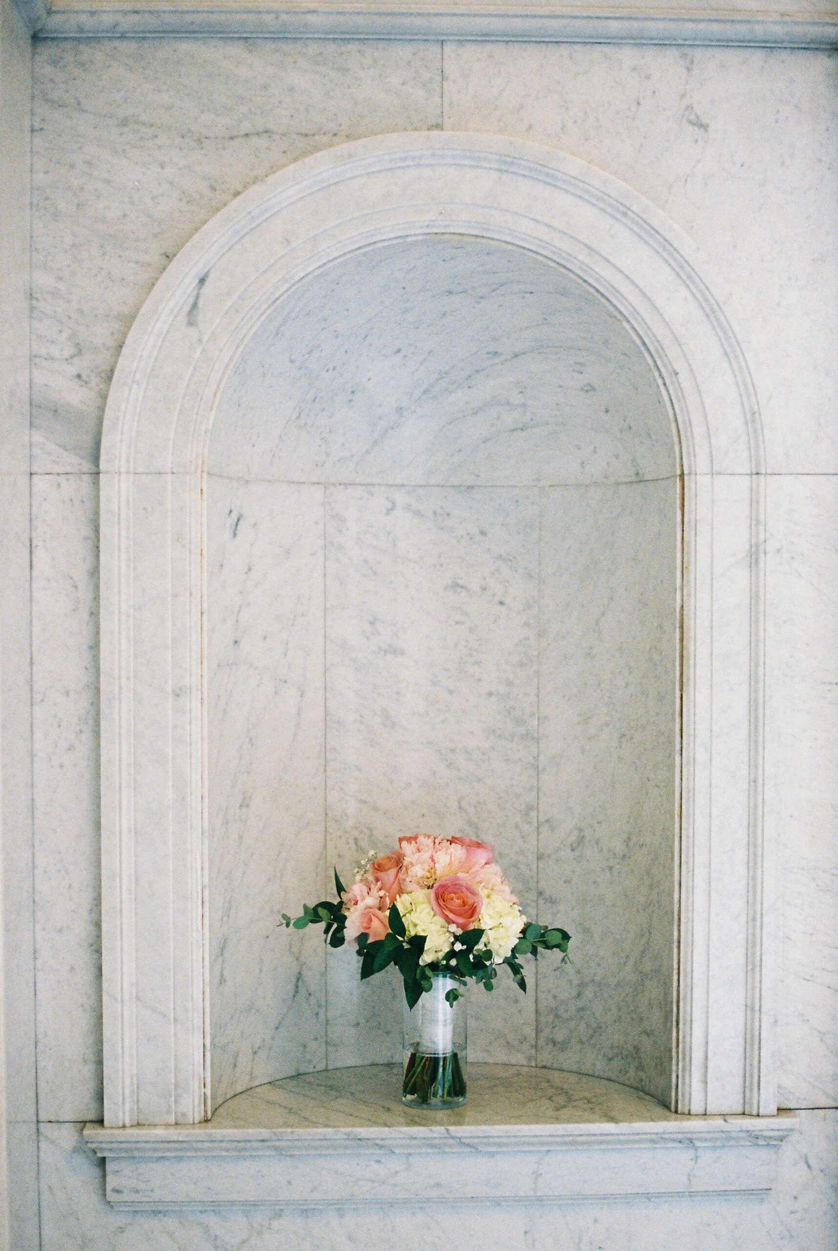 Pink and white bridal bouquet displayed in a marble wall niche inside The Loretto wedding venue.