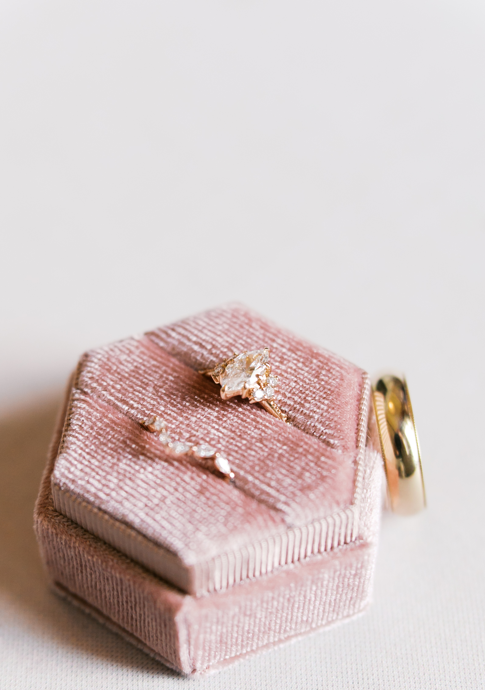 Diamond engagement ring and gold wedding band displayed on a blush velvet ring box before the wedding ceremony.