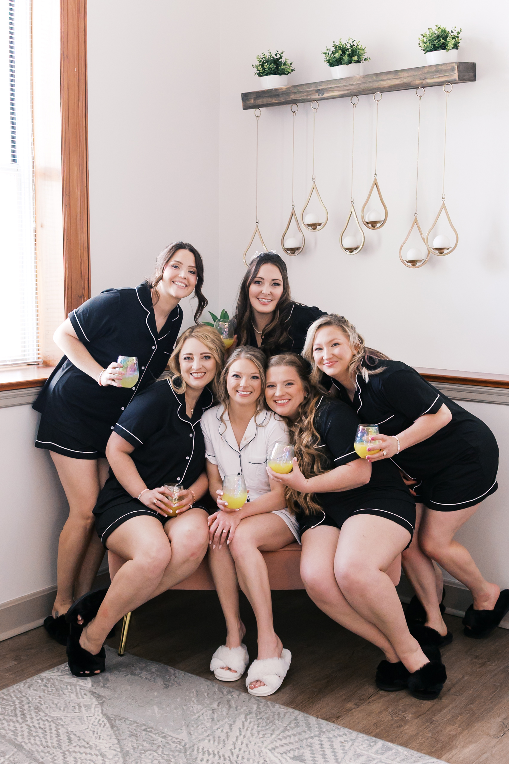 Bride and bridesmaids in matching pajamas gathered together with mimosas during wedding morning preparations.