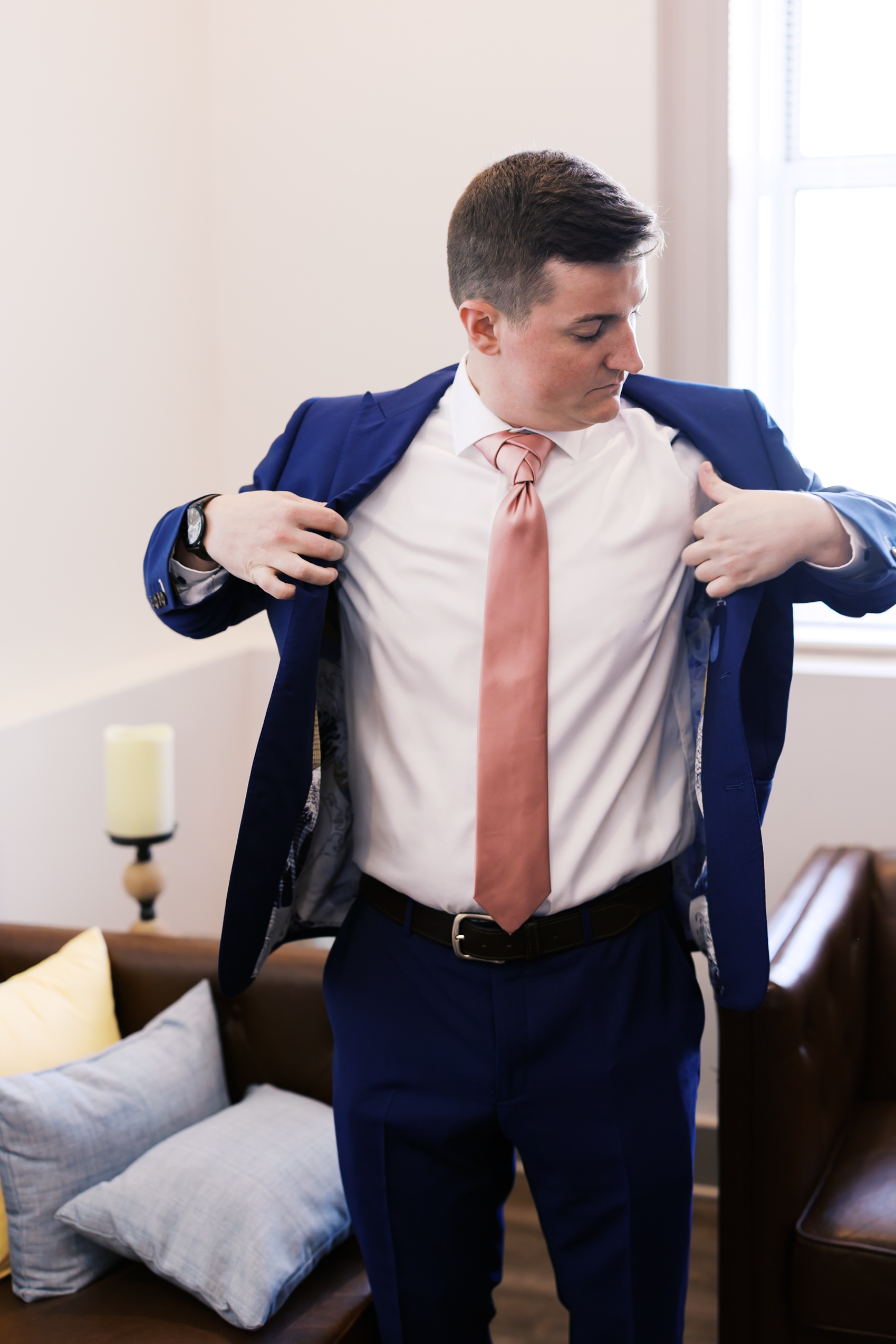 Groom putting on a royal blue suit jacket with a blush pink tie before the wedding ceremony