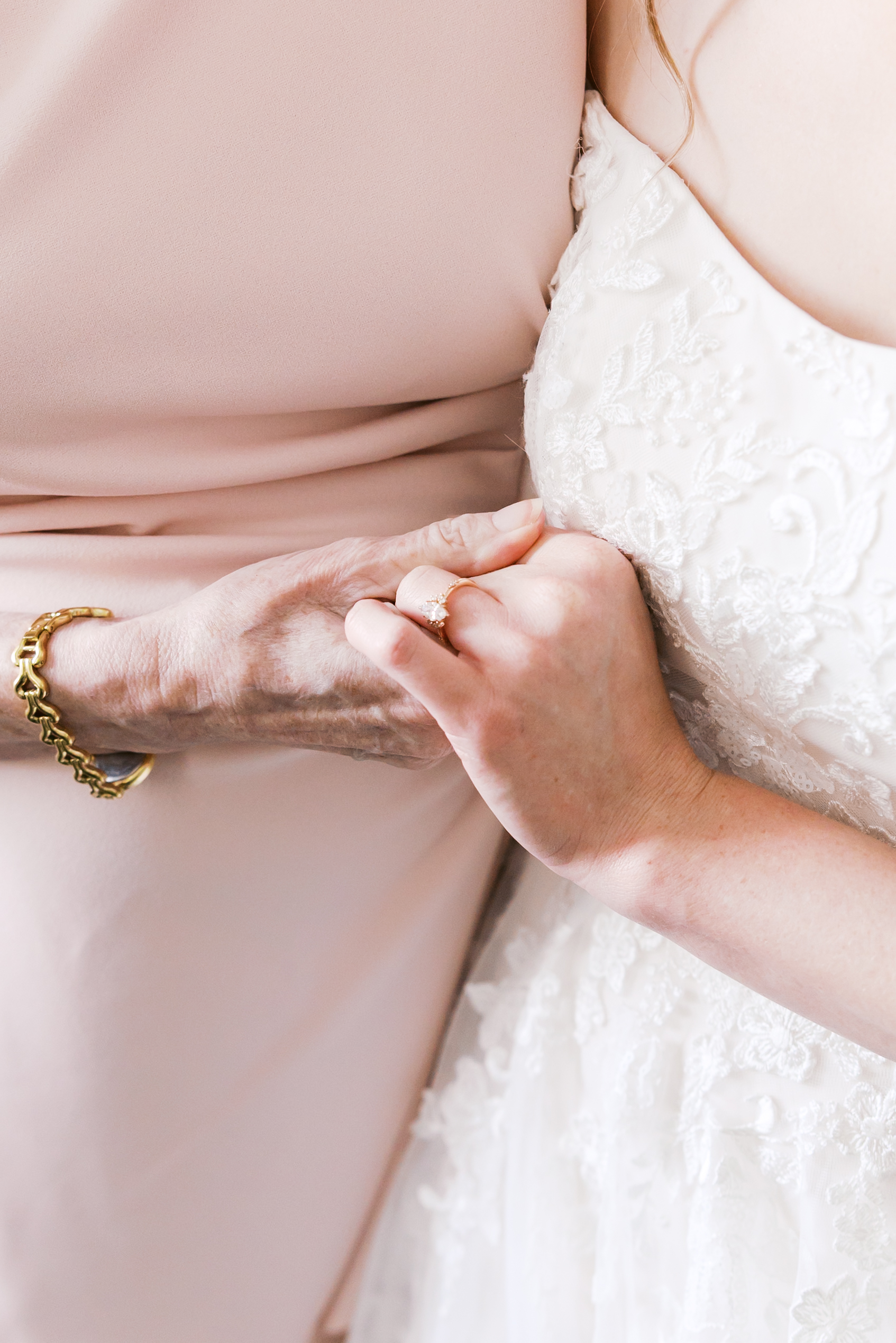 Close-up of the bride holding her mother's hand, featuring her diamond engagement ring and lace wedding gown.