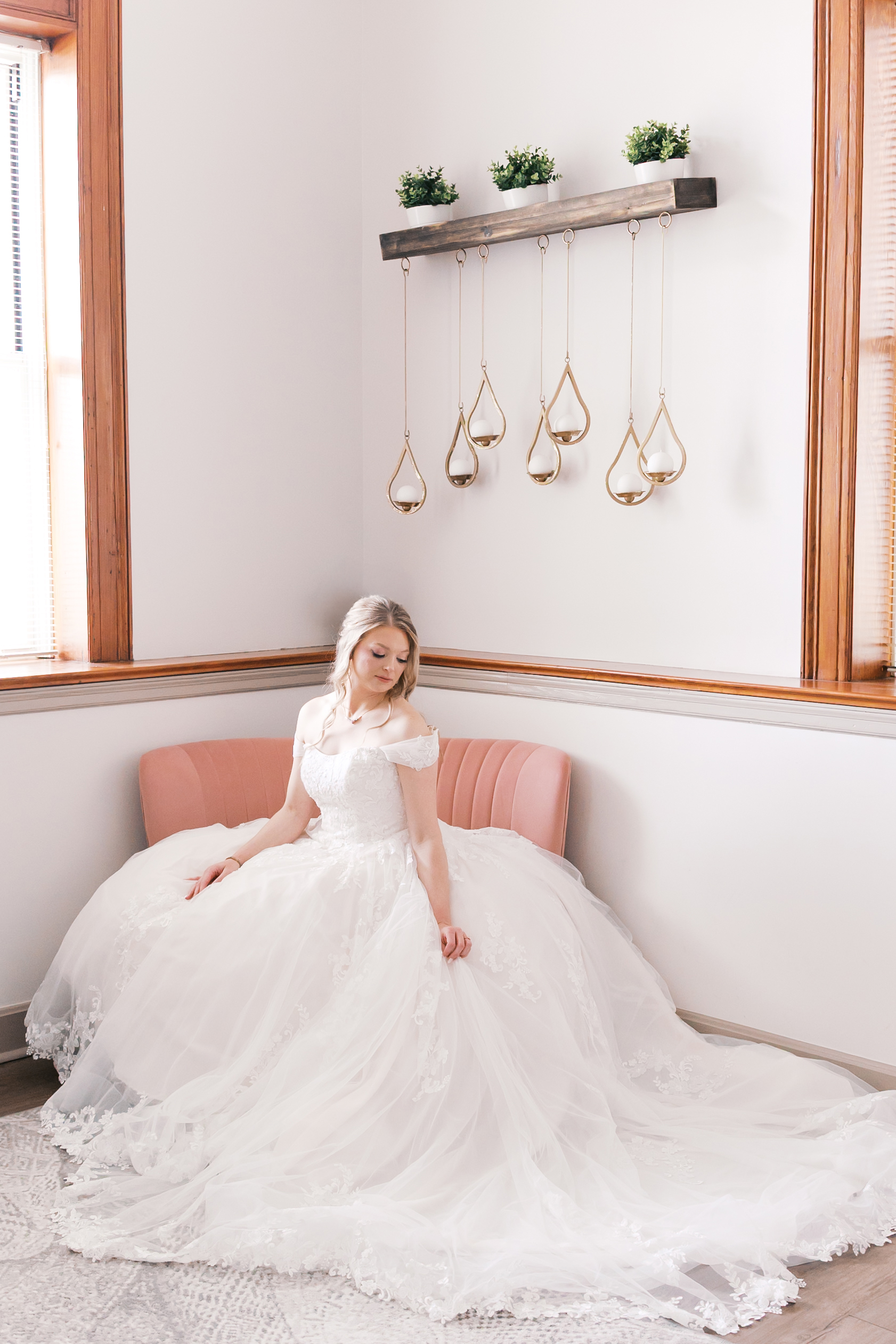 Bride seated on a blush pink loveseat with her full lace wedding gown spread around her.