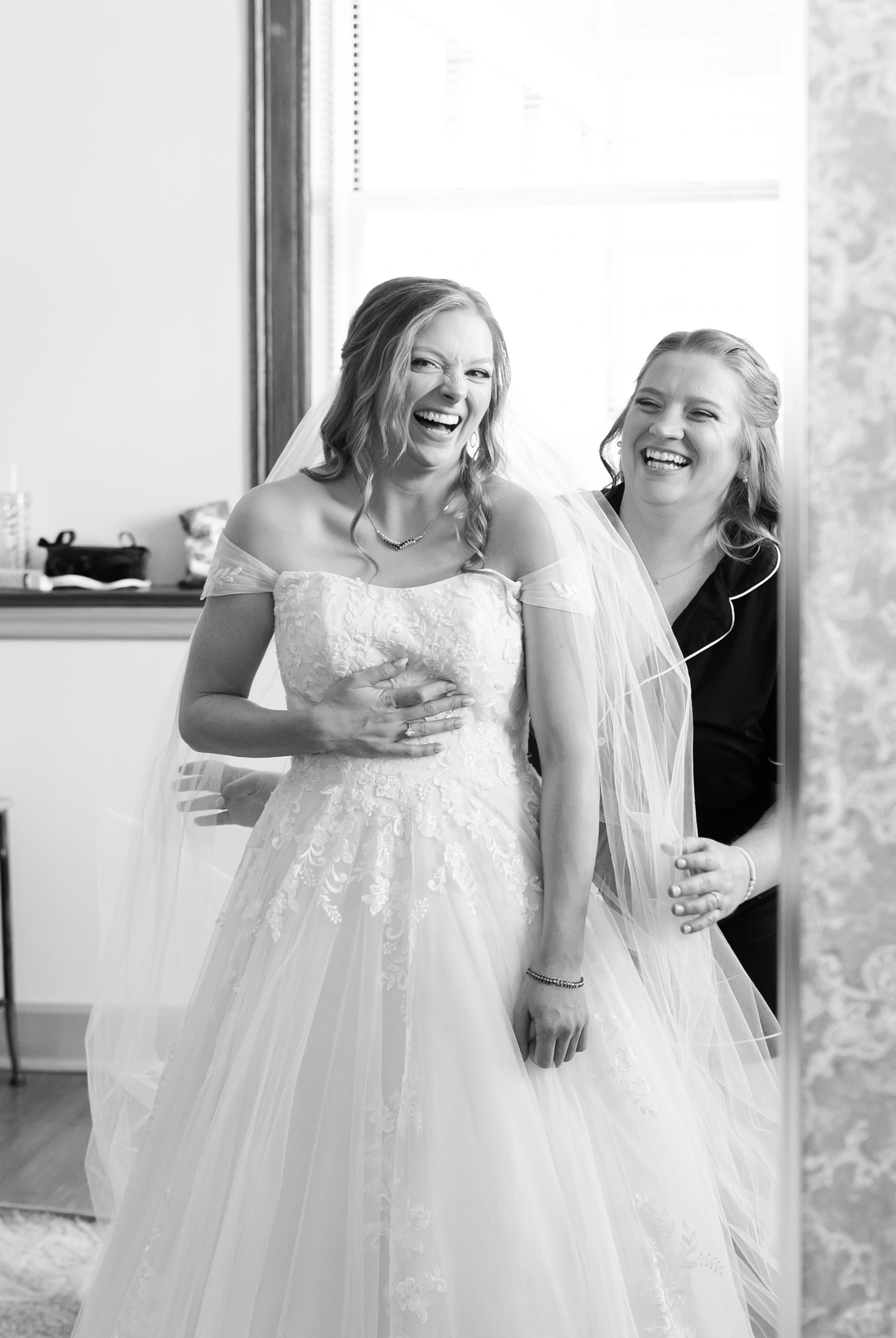 Bride laughing while a bridesmaid adjusts her veil before the wedding ceremony.