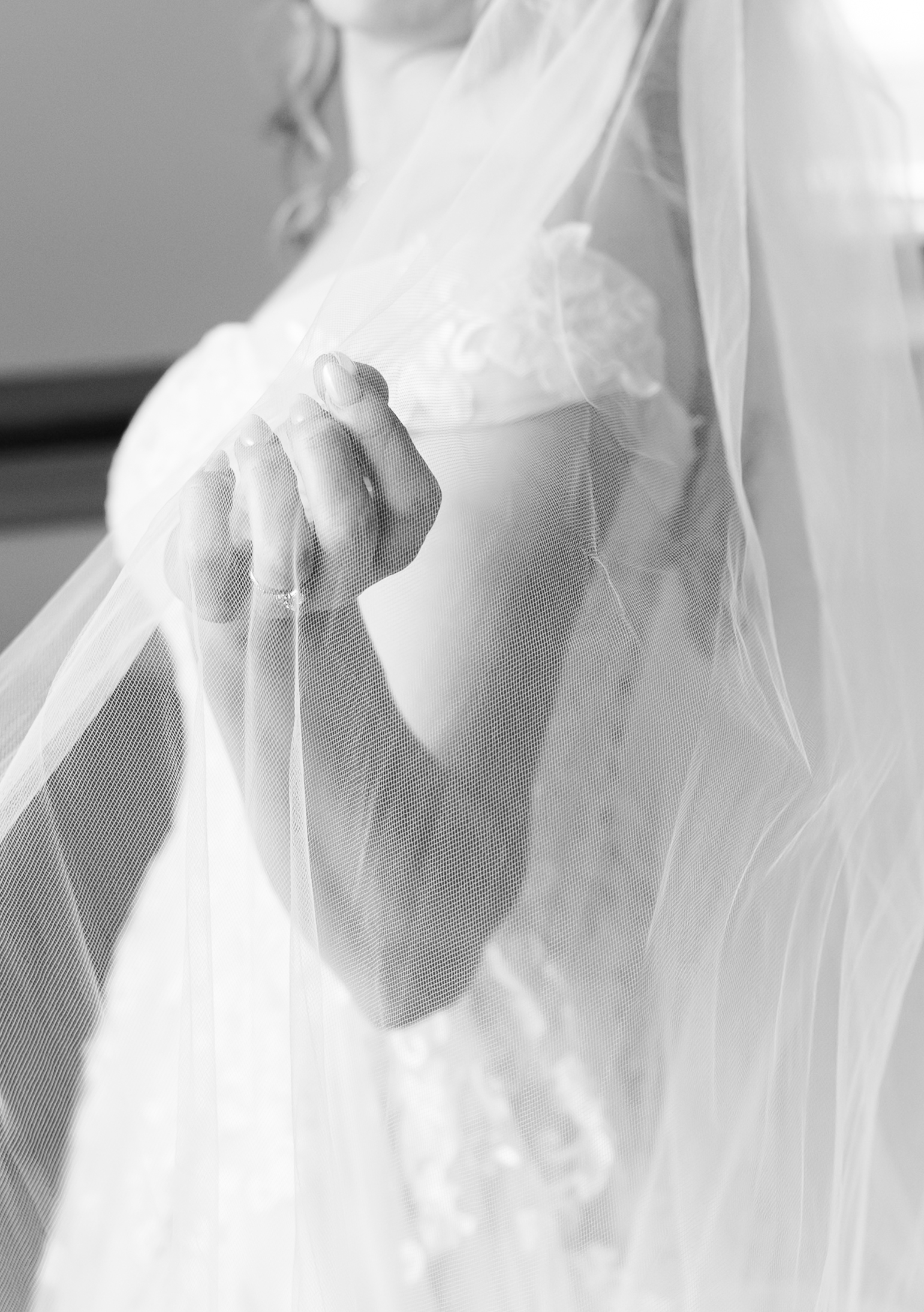 Close-up of a bride holding the edge of her wedding veil over her lace gown.