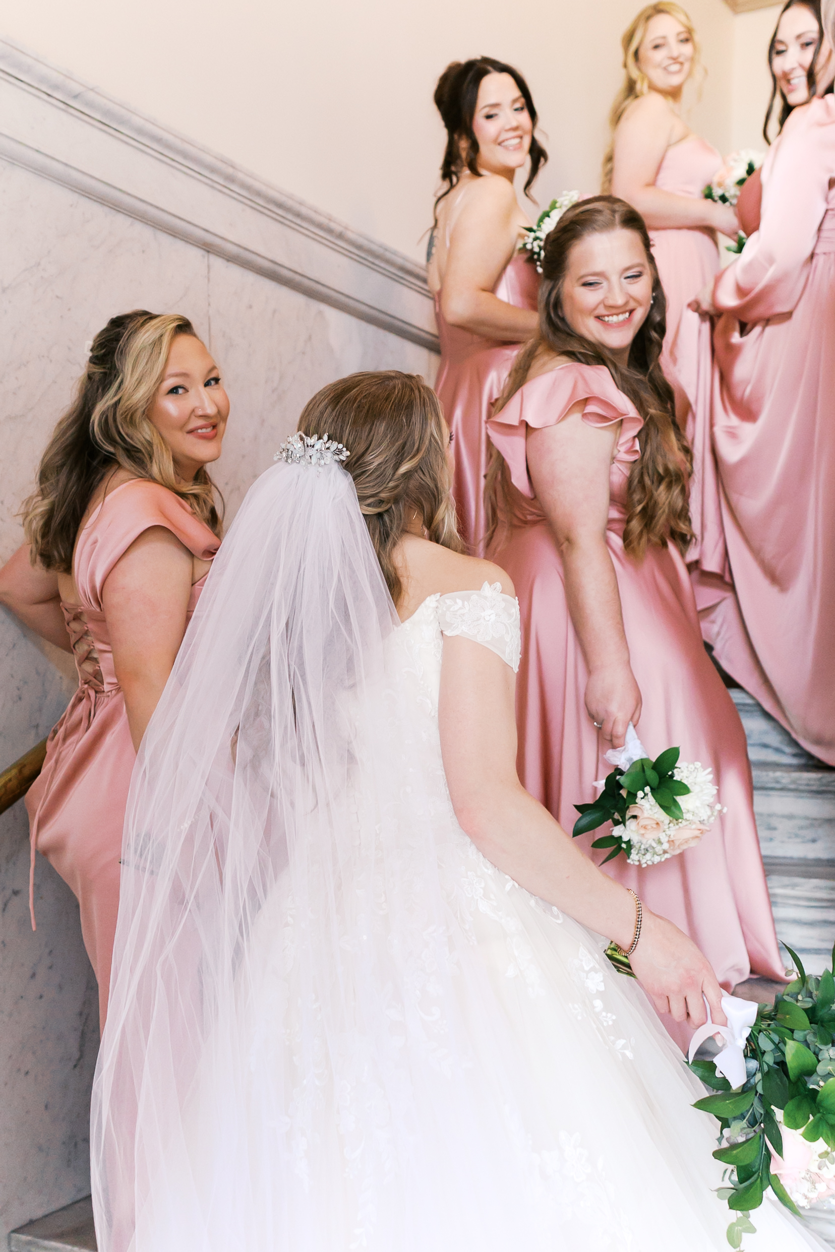 Bride and bridesmaids walking up a marble staircase before the wedding ceremony.
