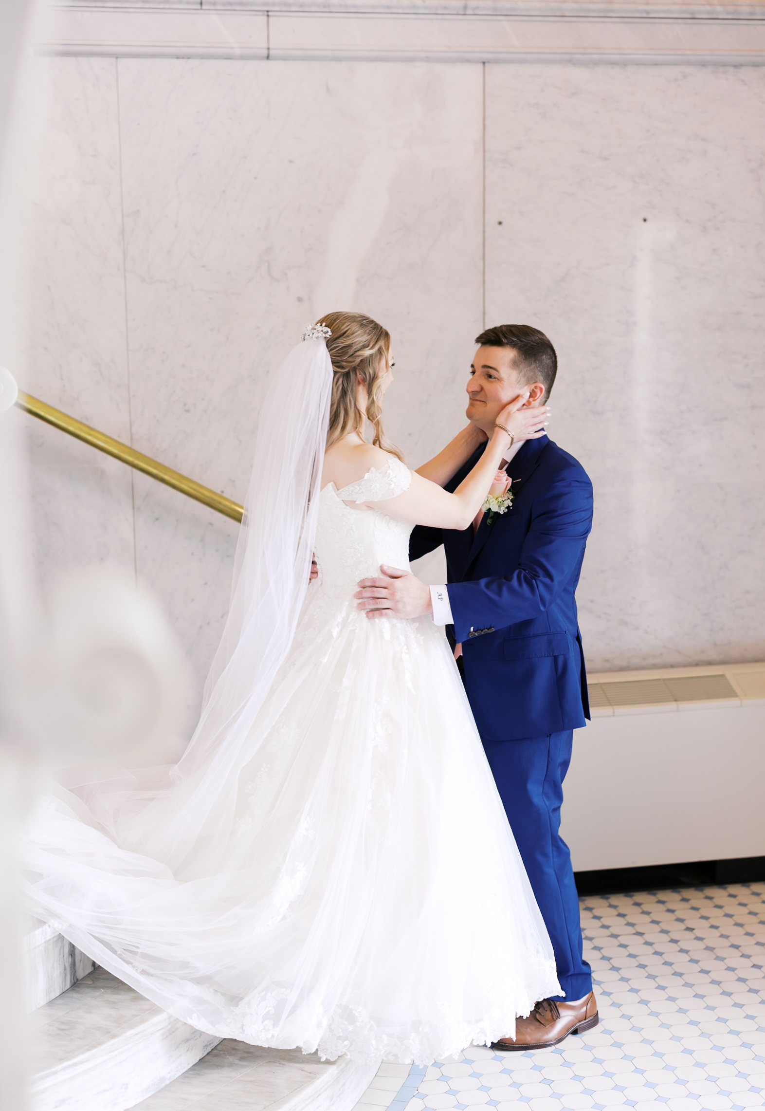 Bride smiling as she embraces the groom during their first look inside a marble stairwell.