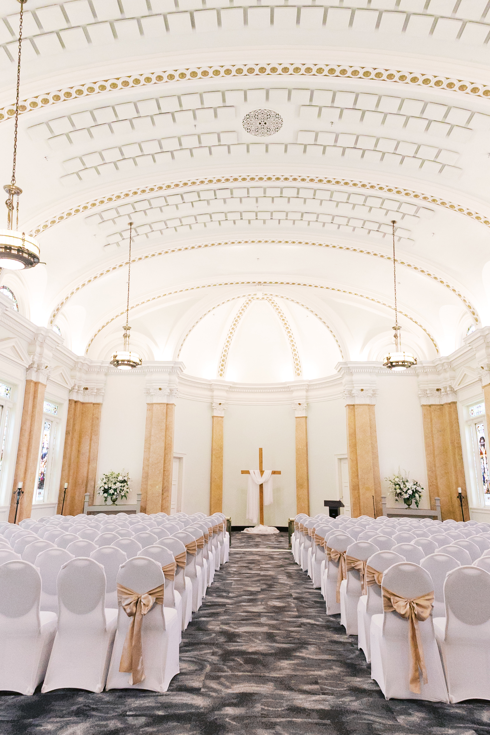 Wedding ceremony space at The Loretto with white-covered chairs, floral arrangements, and a cross at the altar.