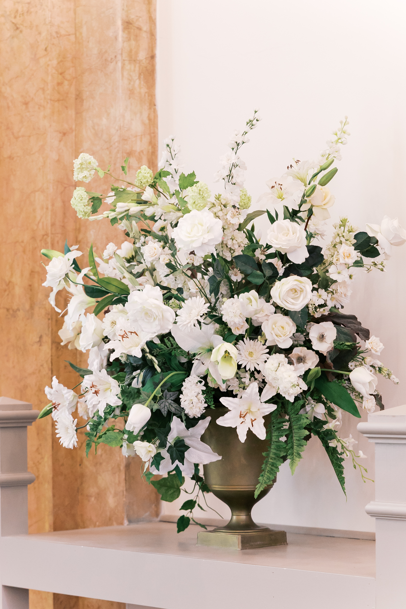 Large white floral arrangement in a gold urn displayed beside the wedding ceremony altar.