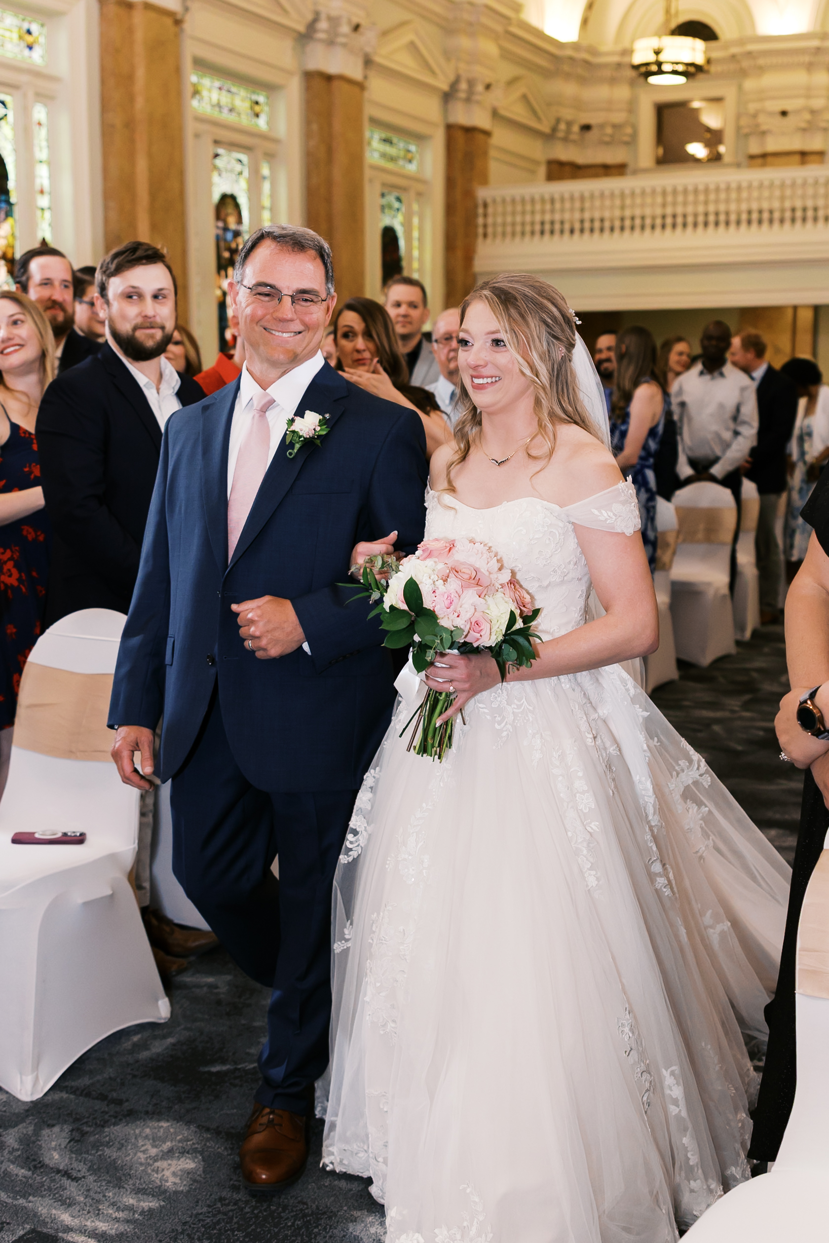 Bride walking down the aisle with her father while holding a pink and white bouquet.