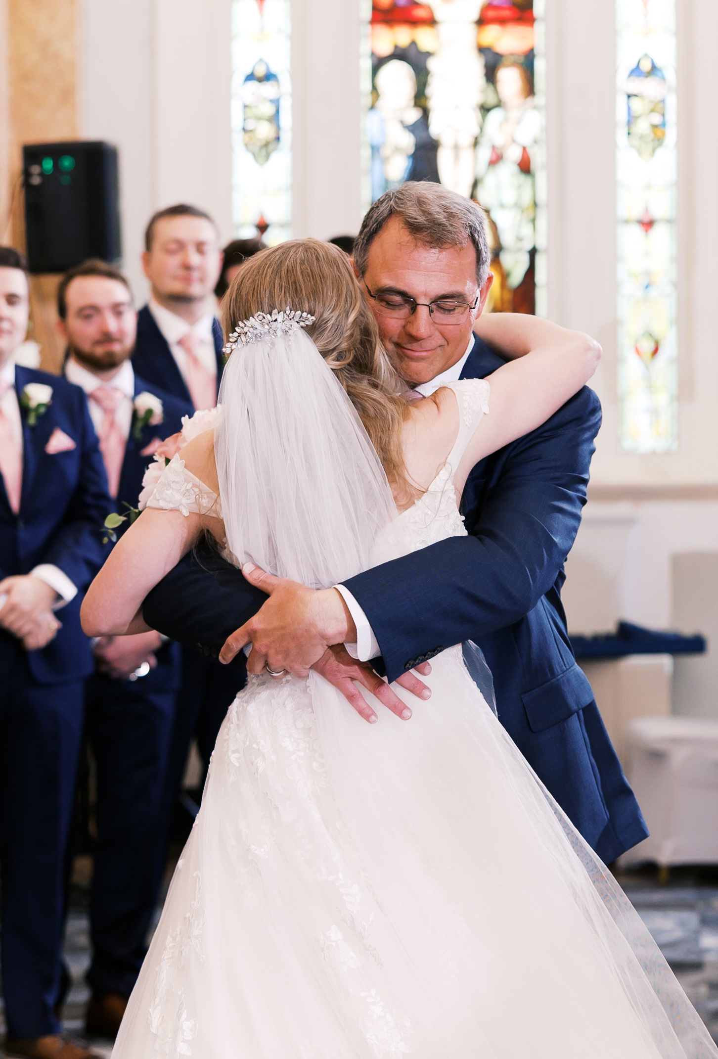 Bride hugging her father during the wedding ceremony as family watches nearby.