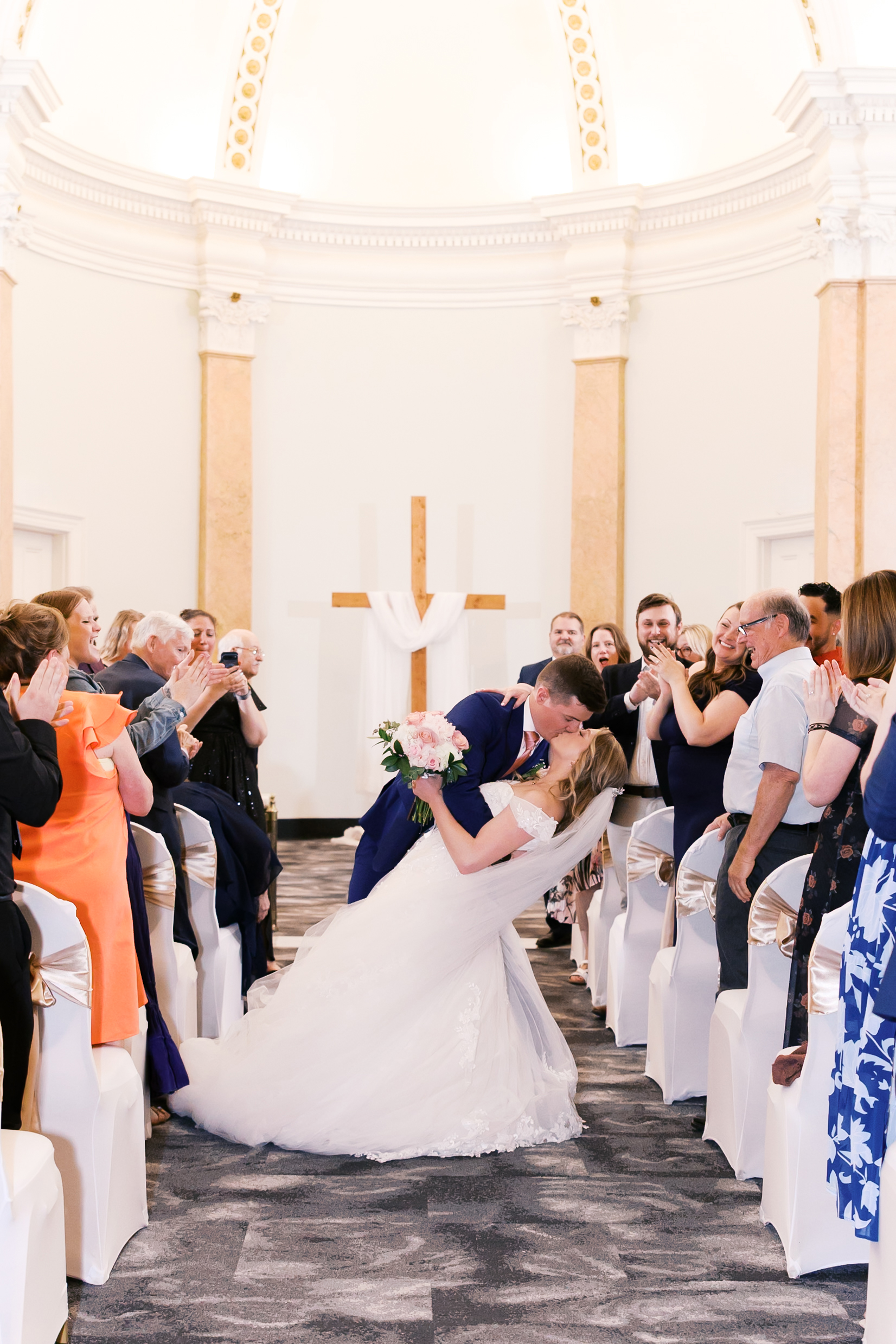 Bride and groom celebrating with a dip kiss as guests applaud after the ceremony.