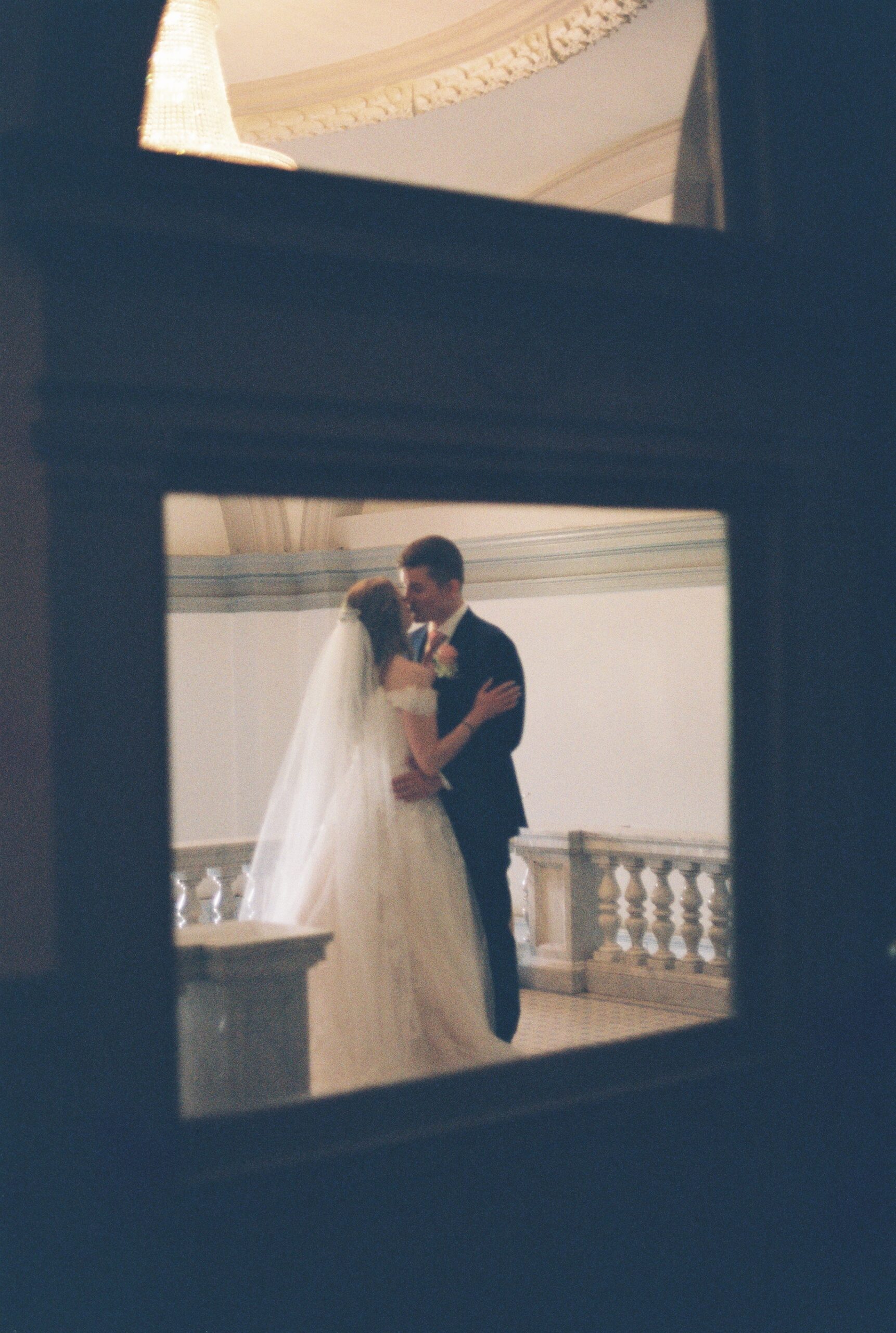 Bride and groom embracing in a softly lit portrait framed through a doorway after the ceremony.