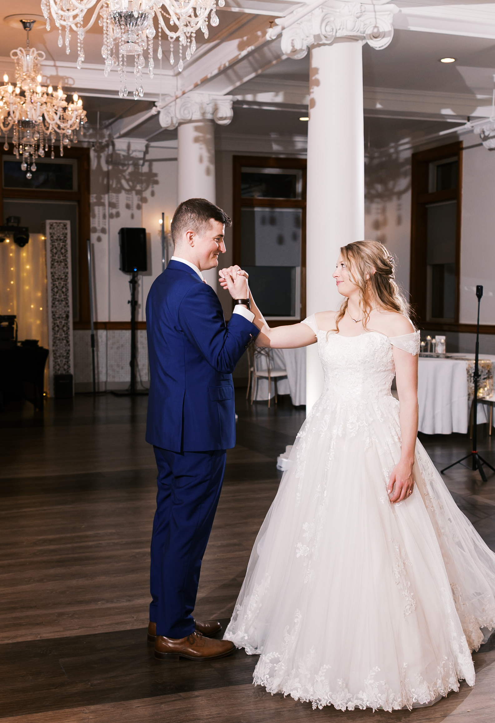 Bride and groom share their first dance beneath crystal chandeliers in an elegant wedding reception ballroom.