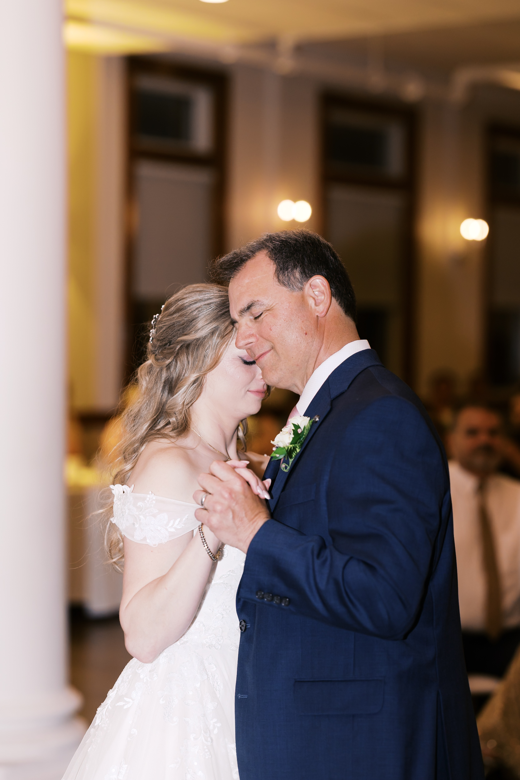 Bride dances with her father during the wedding reception in a softly lit ballroom.