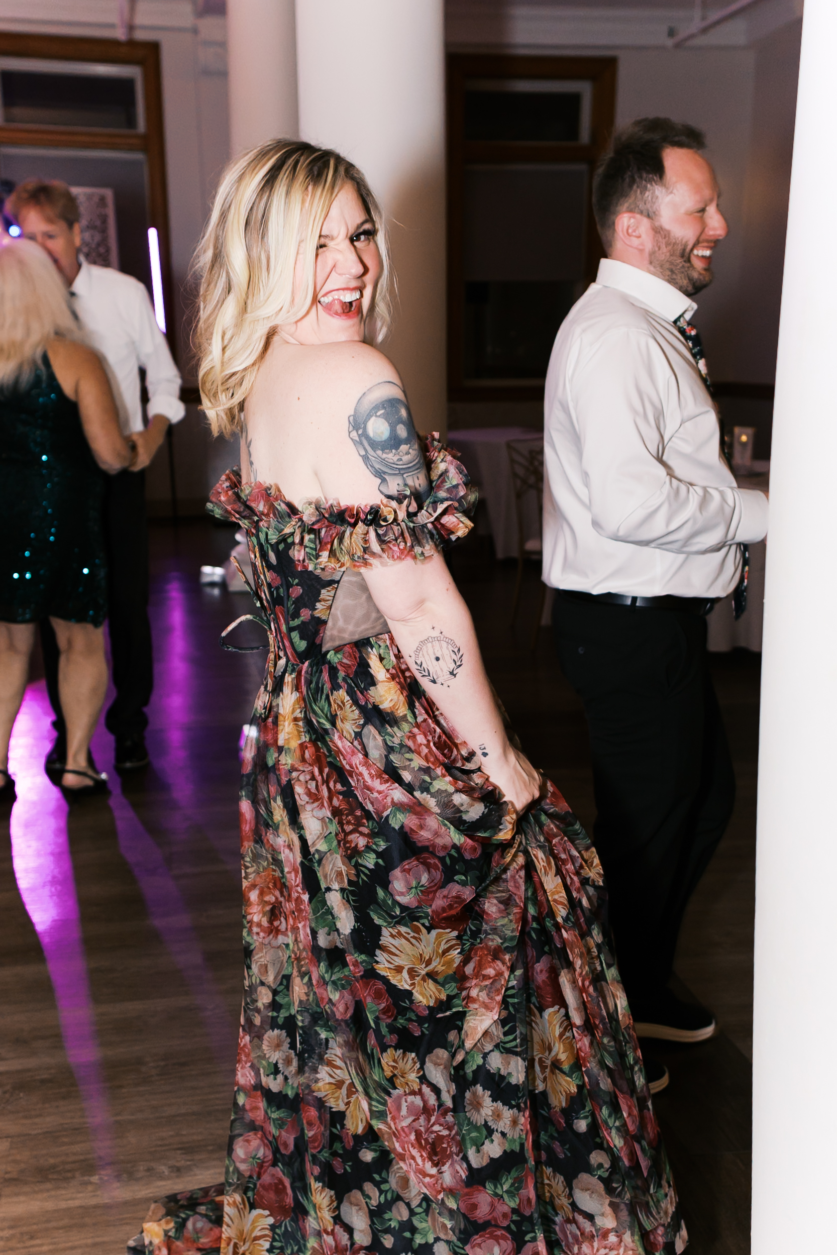 Wedding guest in a colorful floral dress dances and smiles during a lively reception celebration.