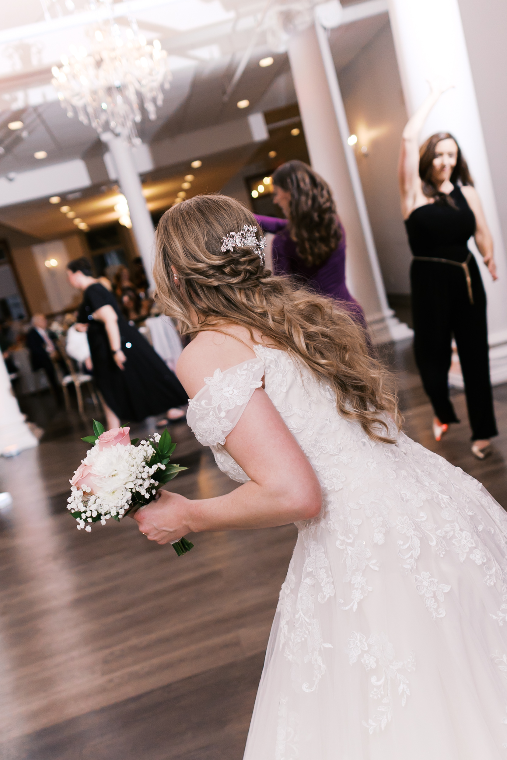 Bride tosses her bouquet toward wedding guests gathered on the reception dance floor.