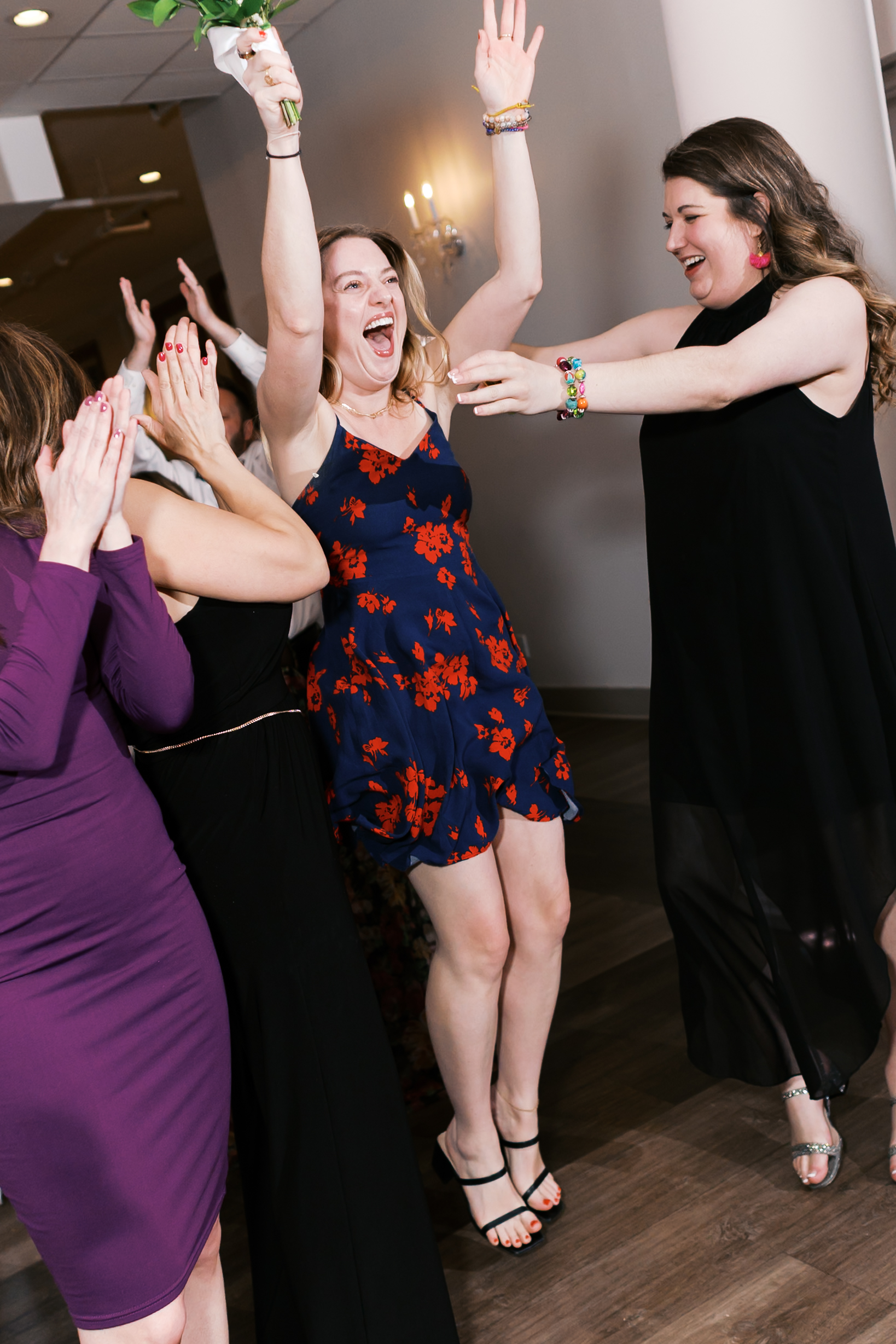 Wedding guest jumps to catch the bridal bouquet as friends cheer during the bouquet toss.