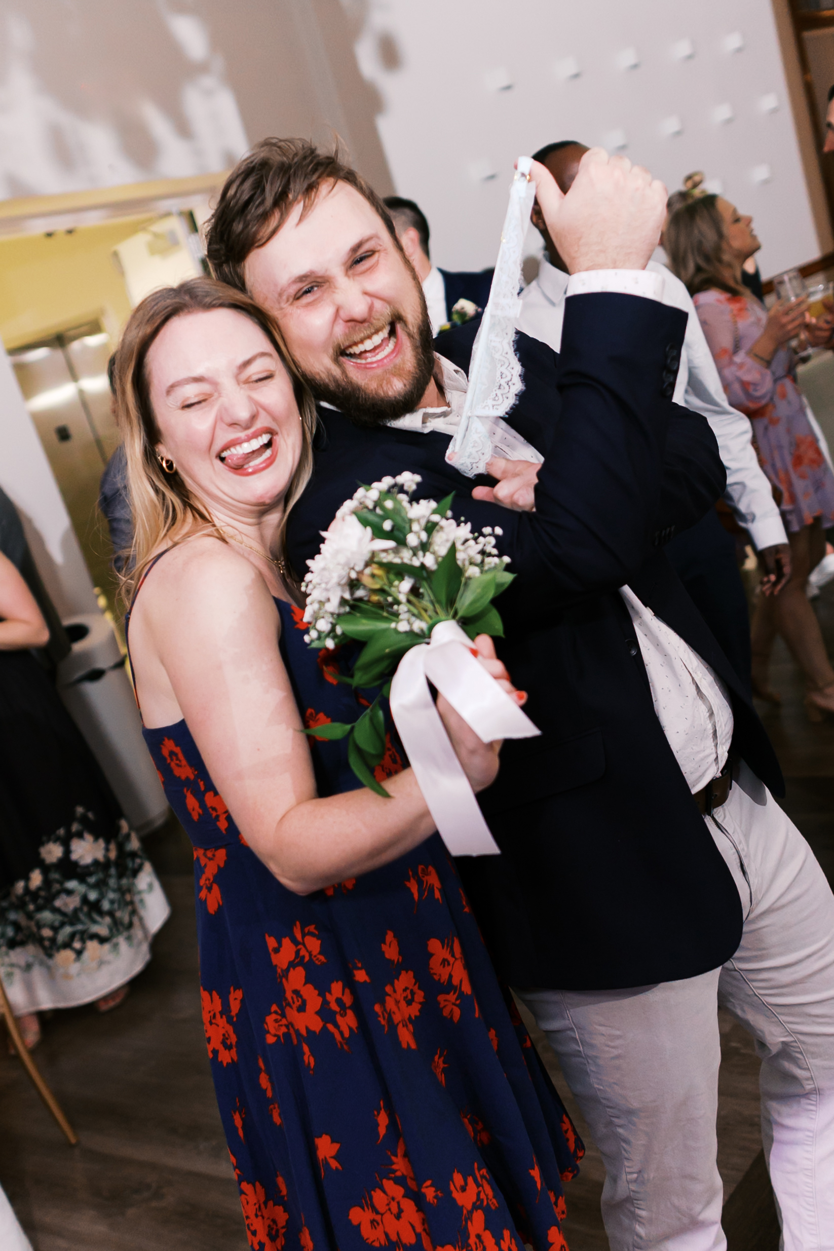 Bouquet and garter toss winners celebrate together, holding the bouquet and garter while laughing on the reception dance floor.
