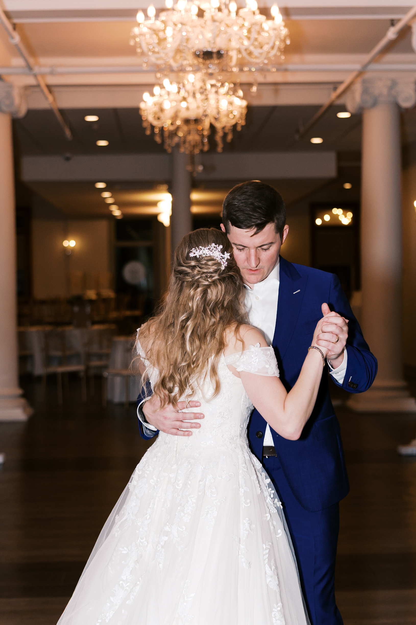Bride and groom dance together at their wedding reception beneath elegant chandeliers in a spacious ballroom.