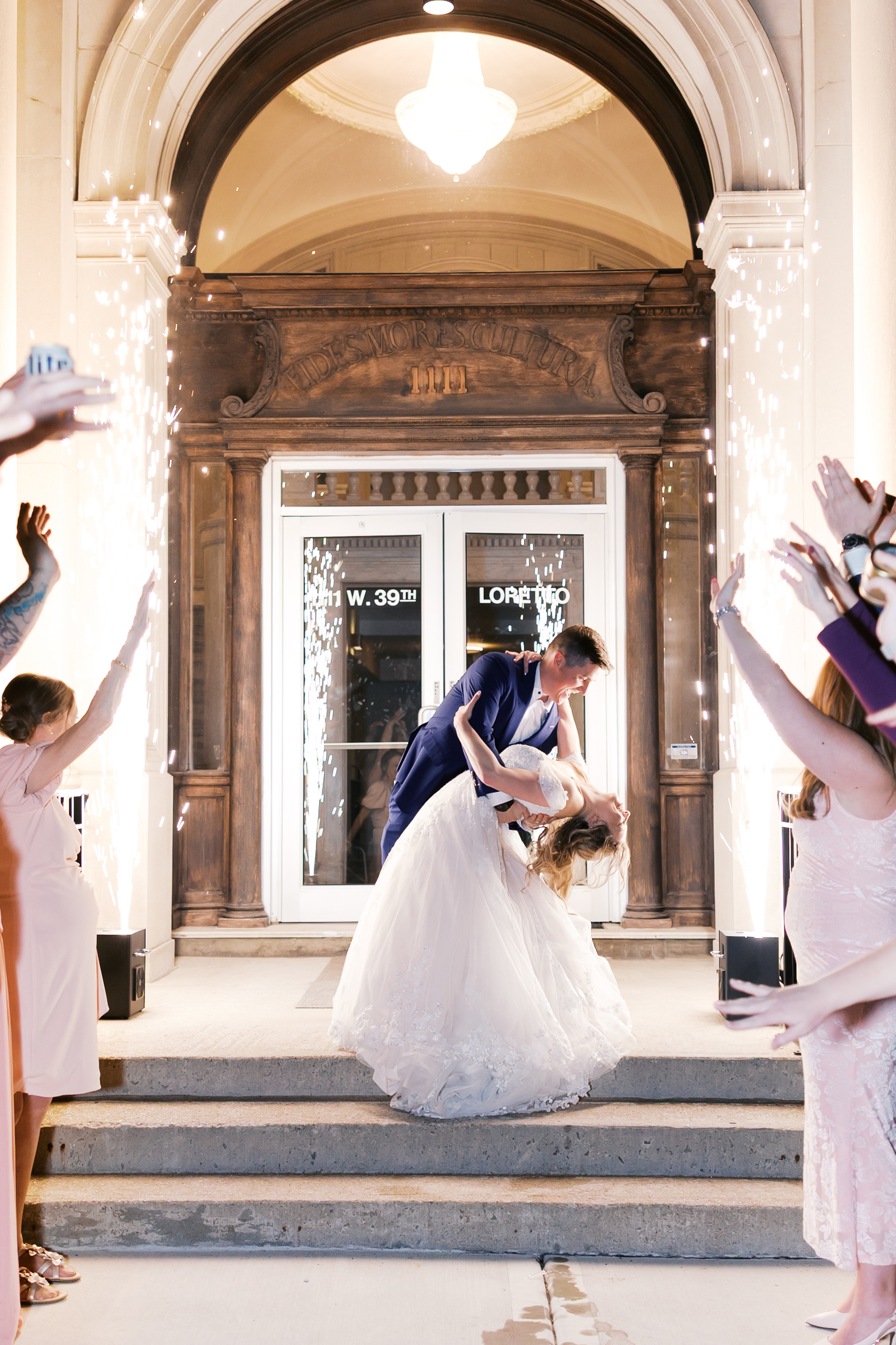 Bride and groom share a dramatic dip kiss beneath sparklers during their wedding send-off outside the reception venue.