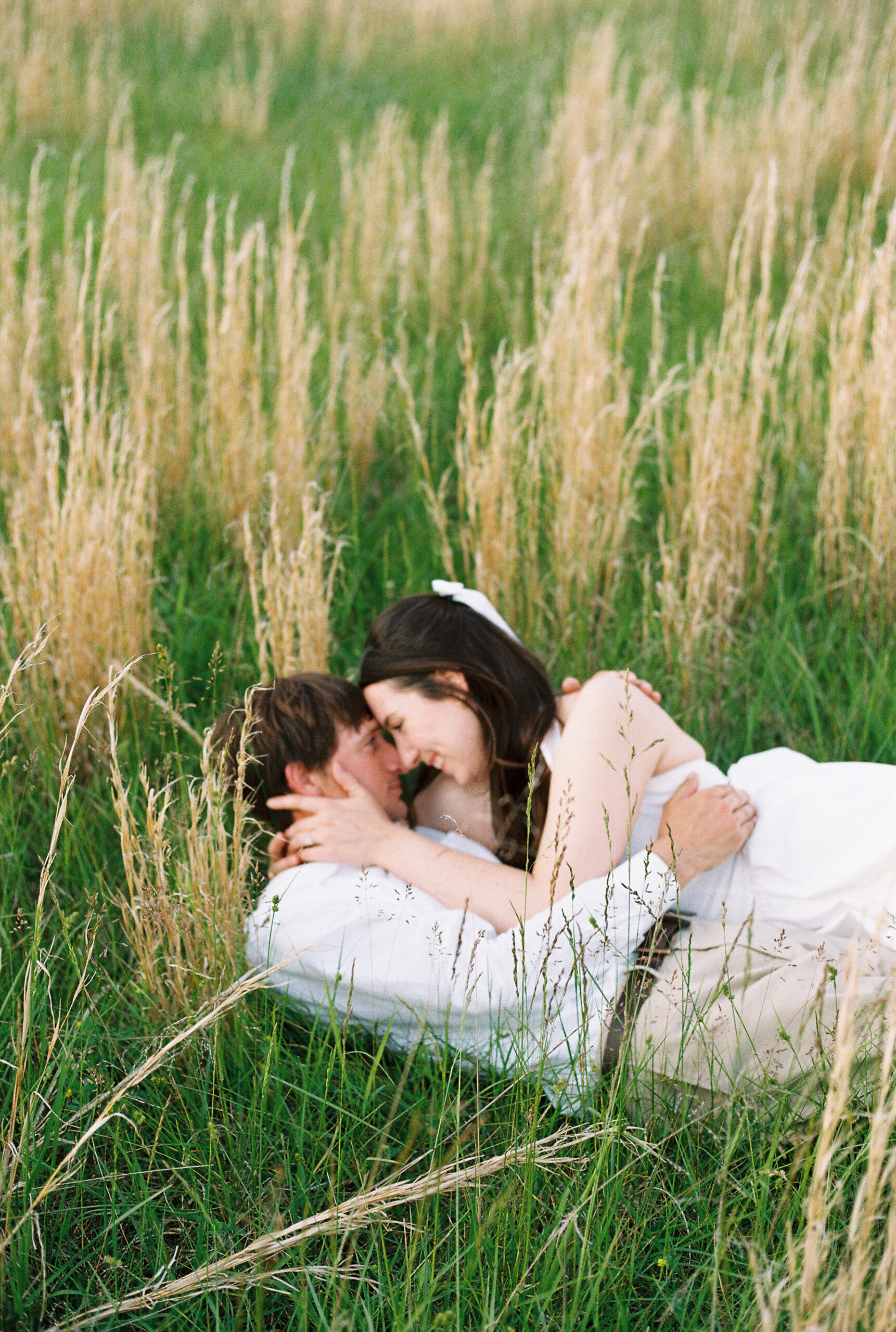 Engaged couple embracing in tall grass at the client's home.