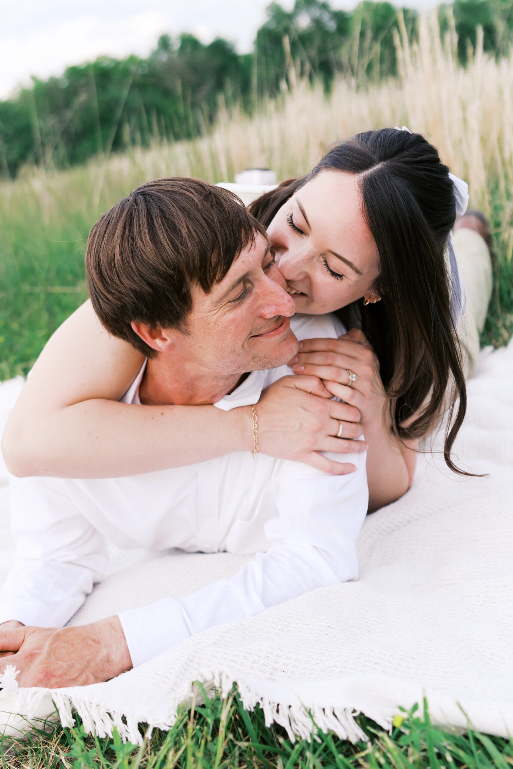 Engaged couple lying on a blanket in the grass, faces close together, at the client's home.