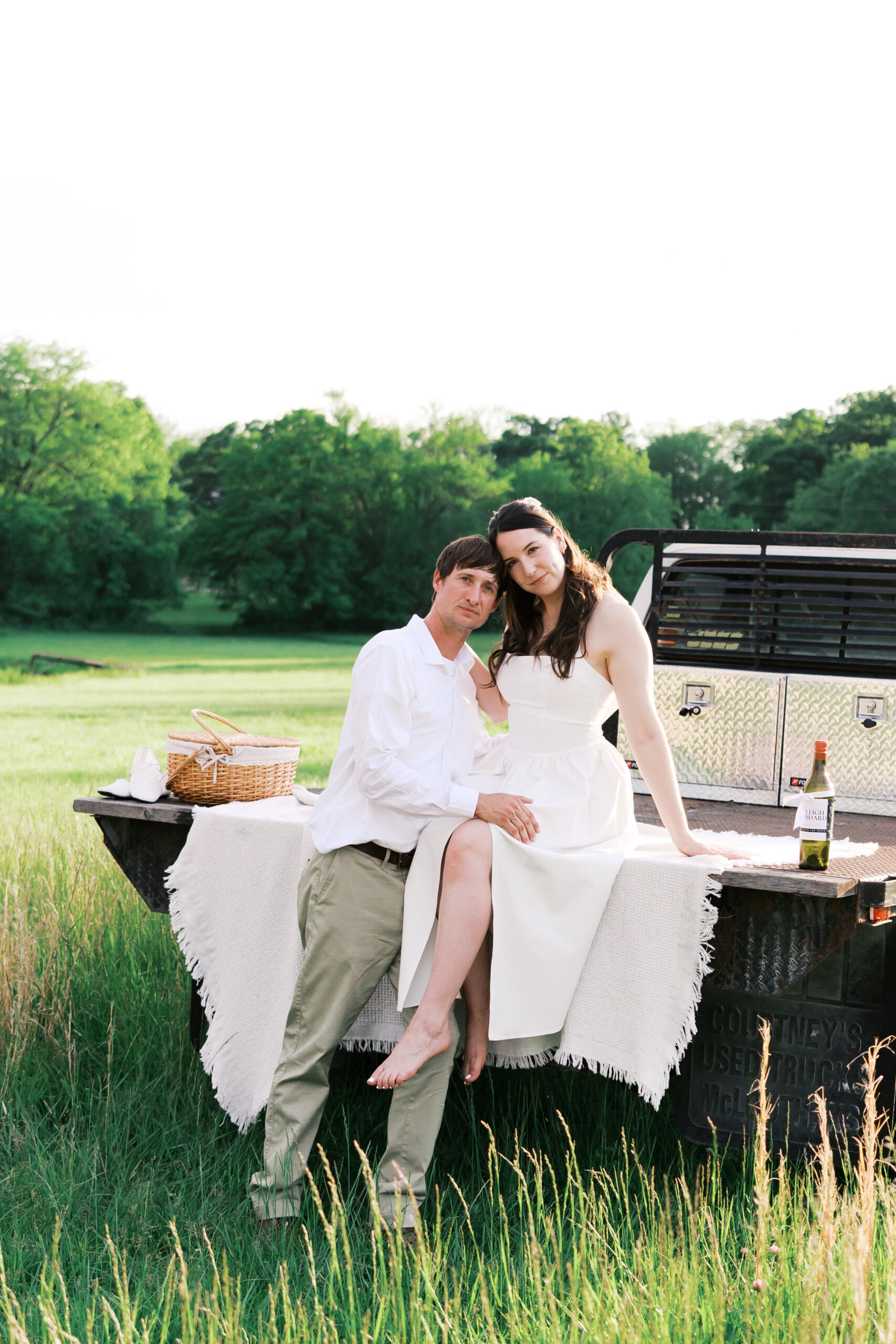 Engaged couple sitting on a truck tailbed with a picnic setup at the client's home.
