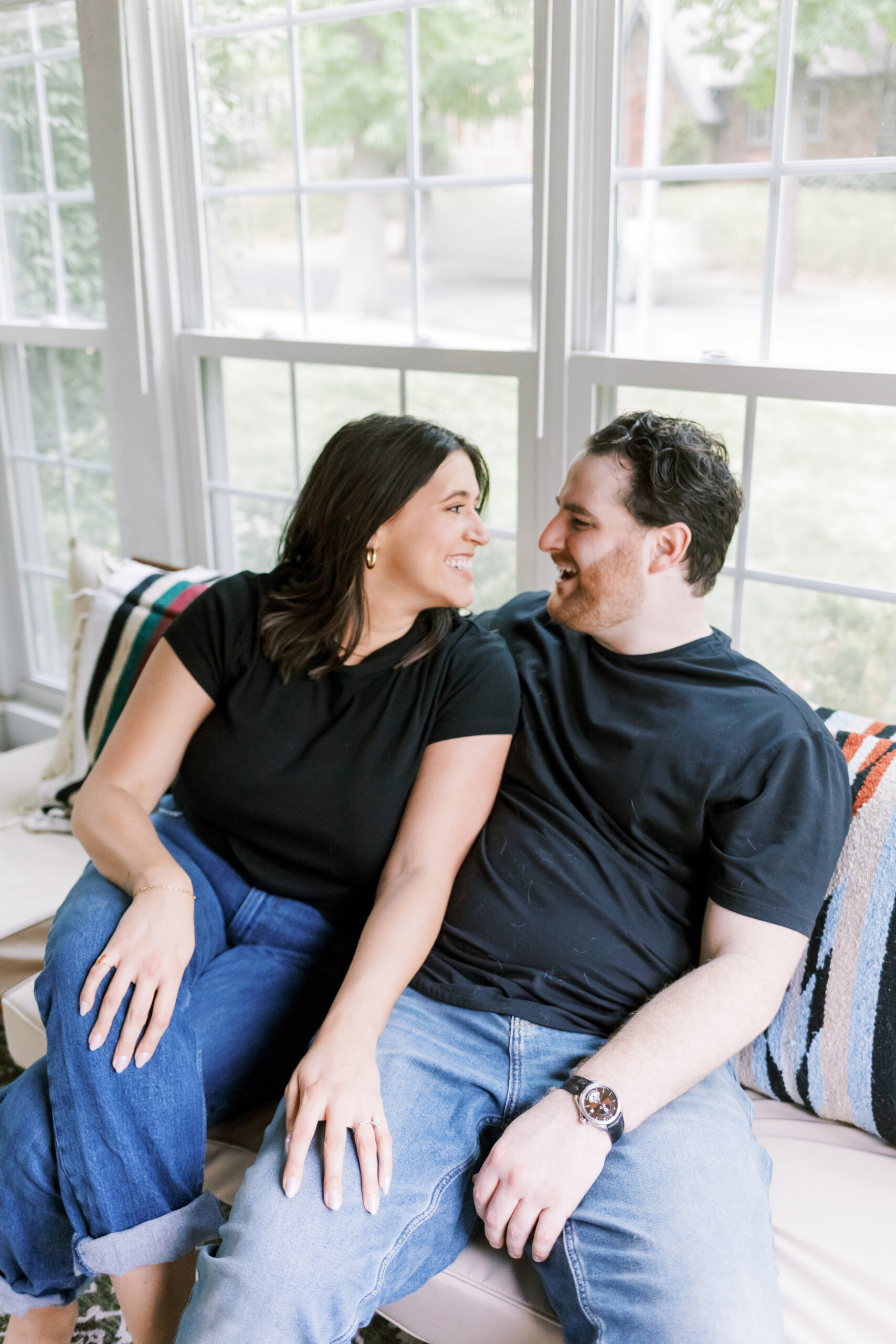 Engaged couple laughing together on a couch at home.