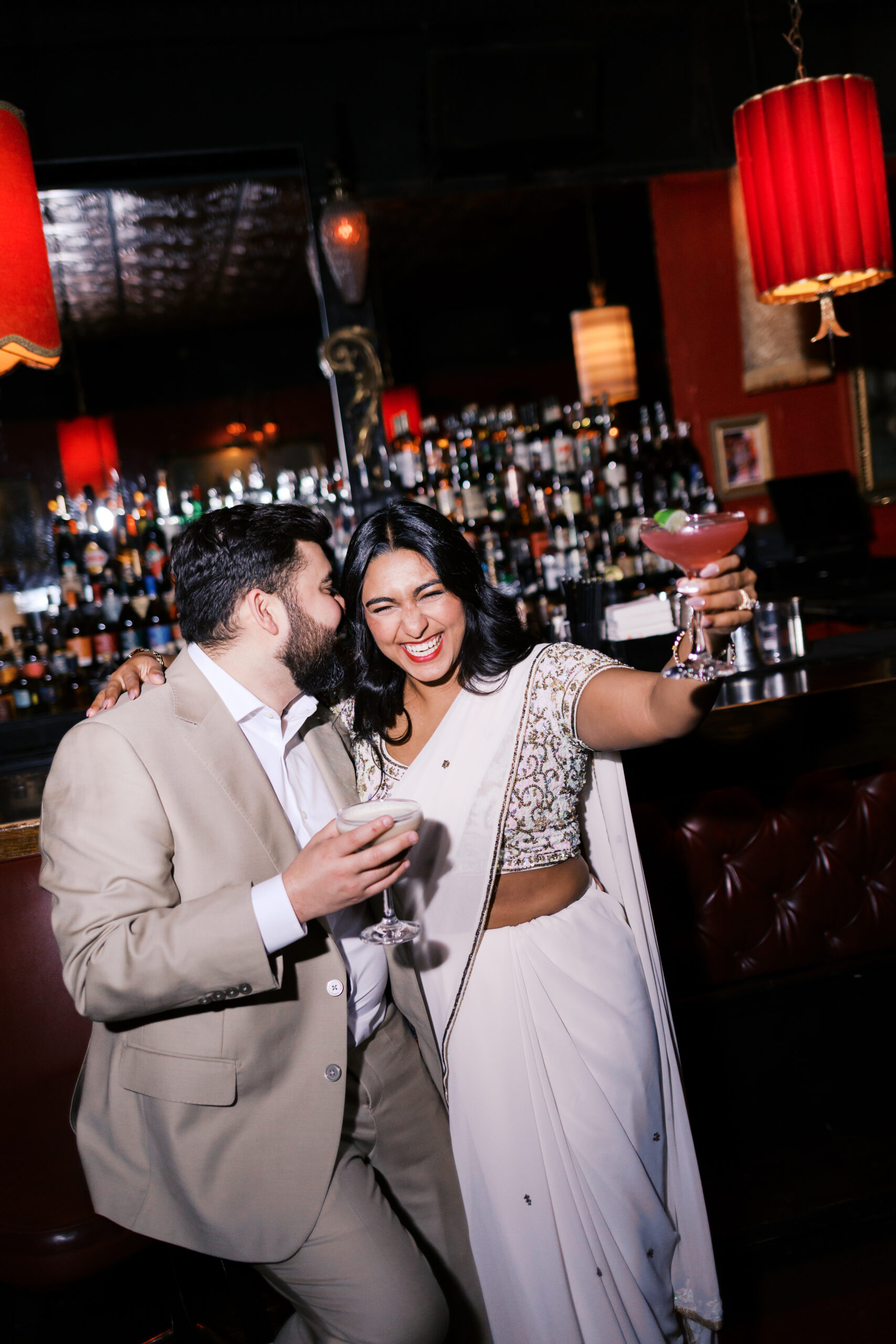 Couple laughing together with cocktails in hand during an engagement session at Green Lady Lounge.