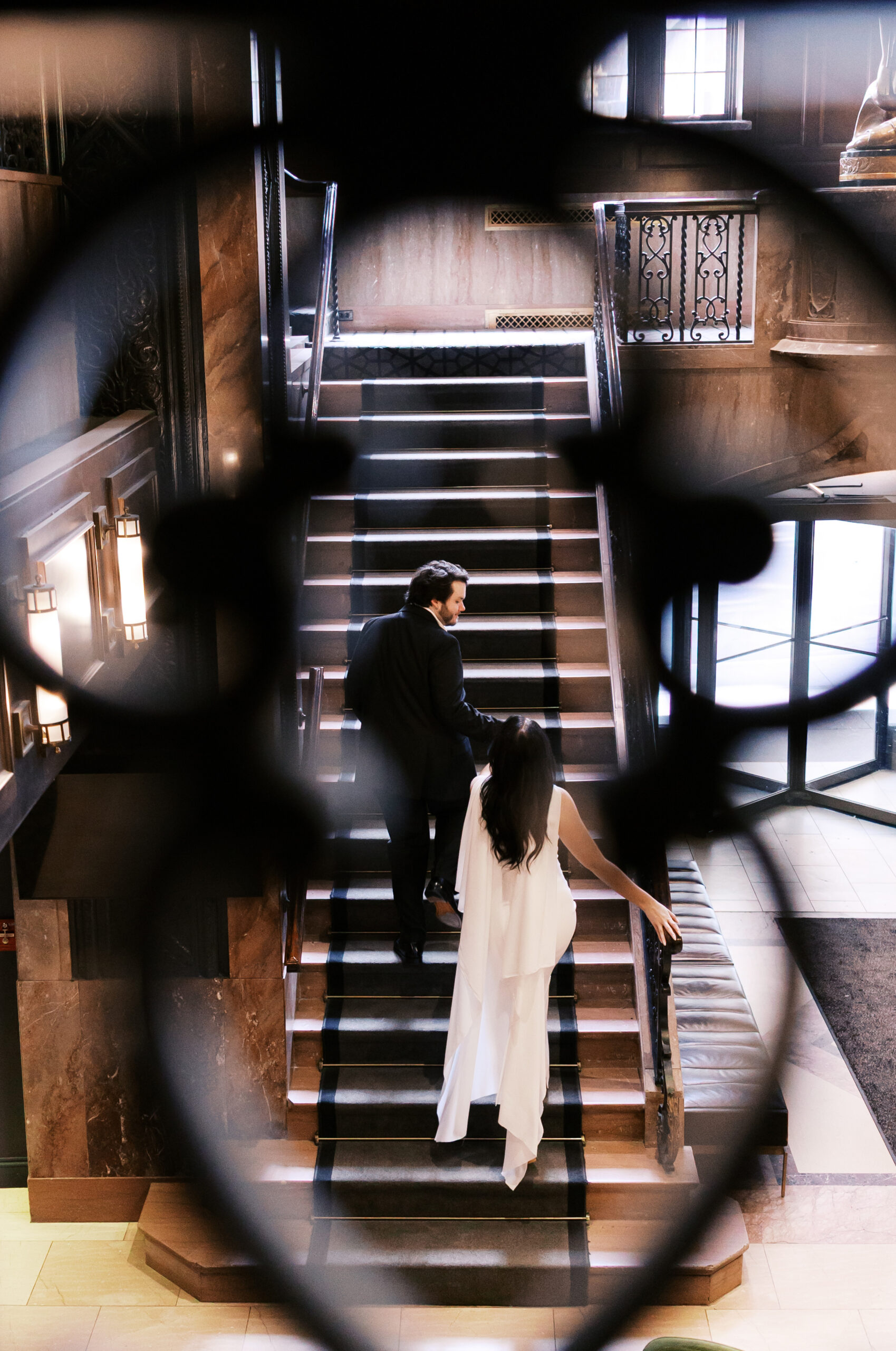 Engaged couple descending a grand staircase at Hotel Phillips, framed by an ornate railing