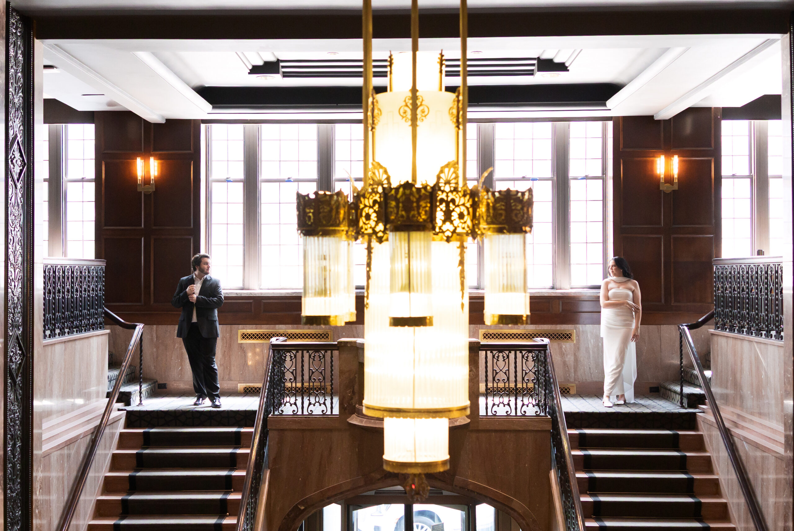 Engaged couple standing on opposite balconies beneath a chandelier at Hotel Phillips.