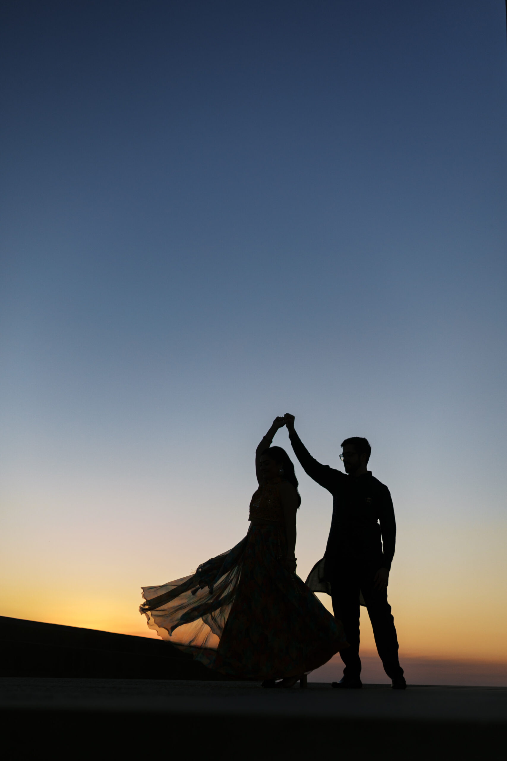 Silhouette of an engaged couple dancing at sunset, her skirt swirling with the twirl.