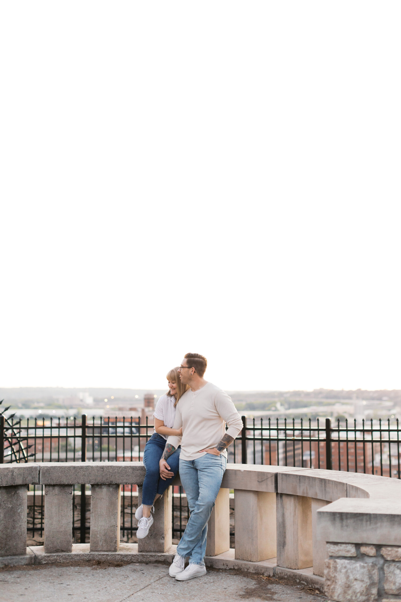 Couple leaning against a stone overlook, city skyline spread out behind them during their engagement session.