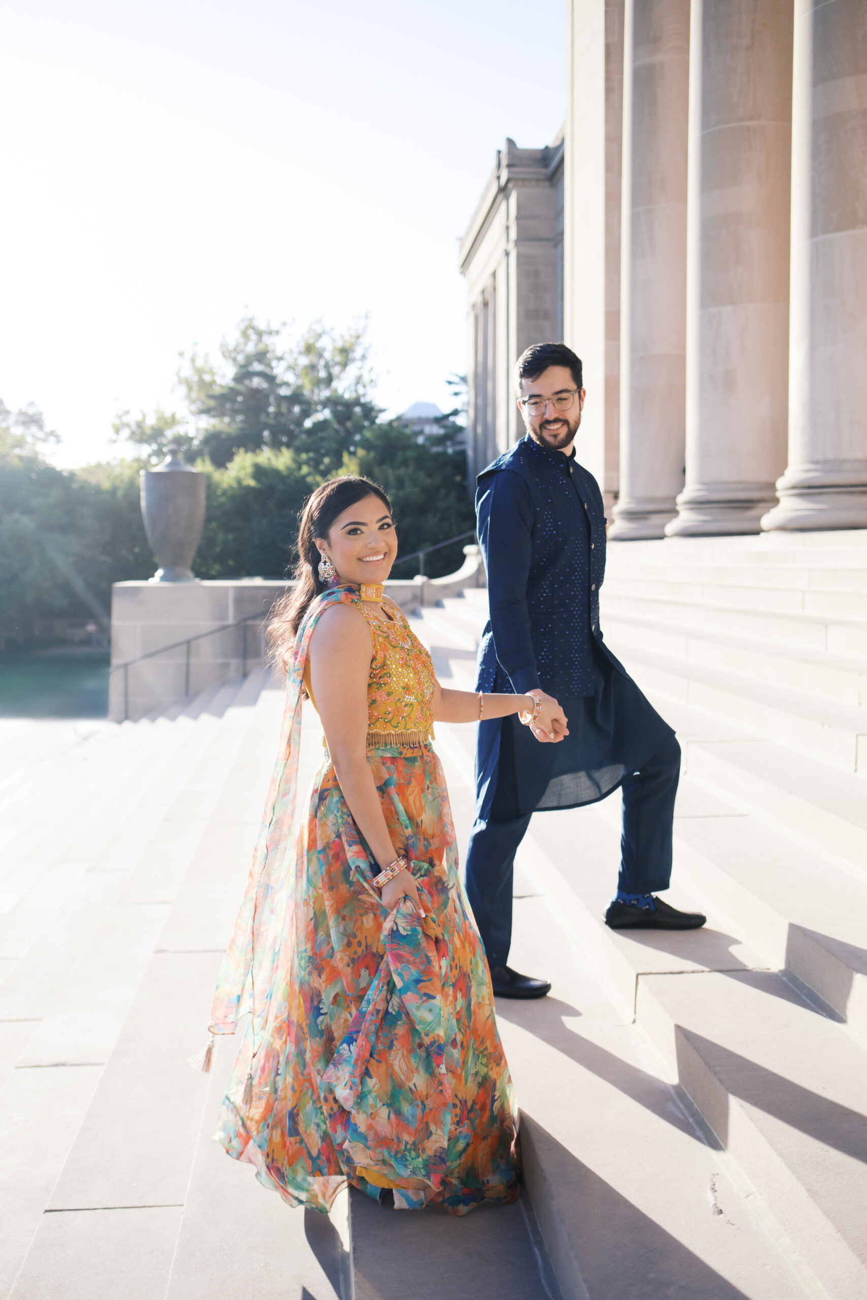 Engaged couple walking down stone steps hand in hand, smiling back at the camera.