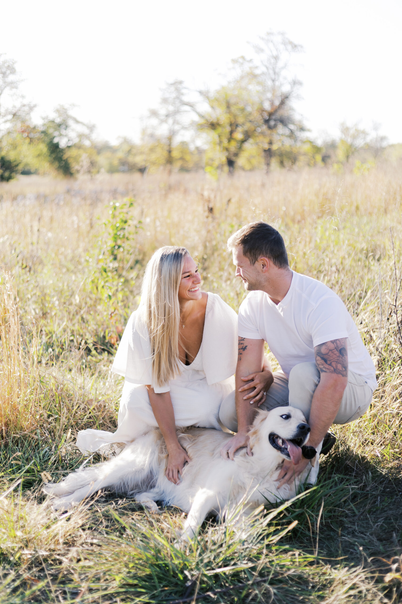 Couple petting their dog together in a sunlit field of tall grass during their Shawnee Mission engagement session.
