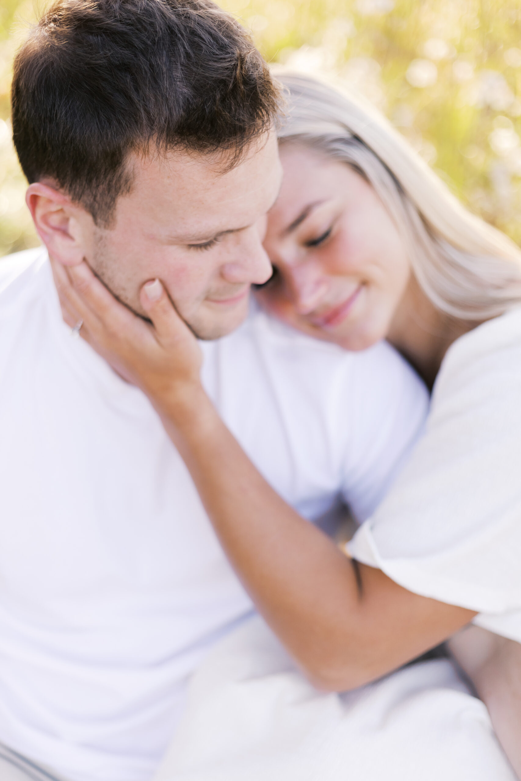 Close-up of an engaged couple embracing, her hand resting on his cheek.