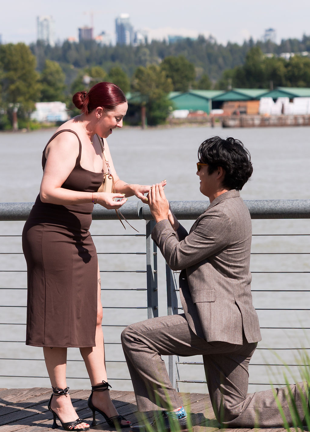 A ring is placed on a finger during the proposal beside the river.