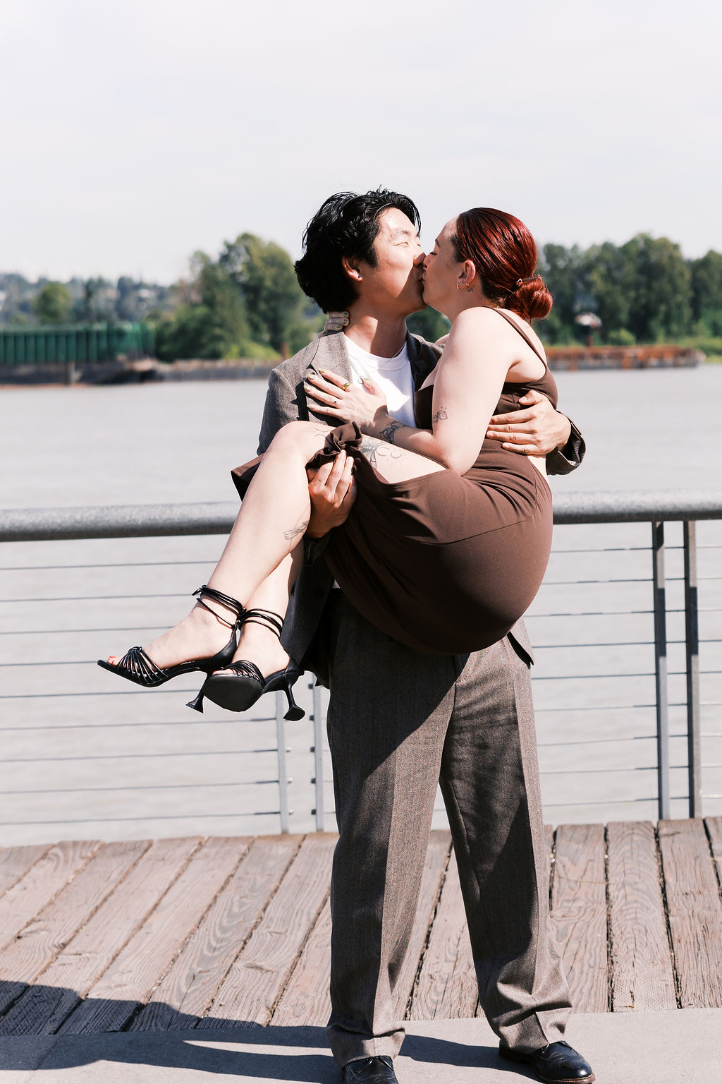 One partner lifts the other during a celebratory kiss by the river.