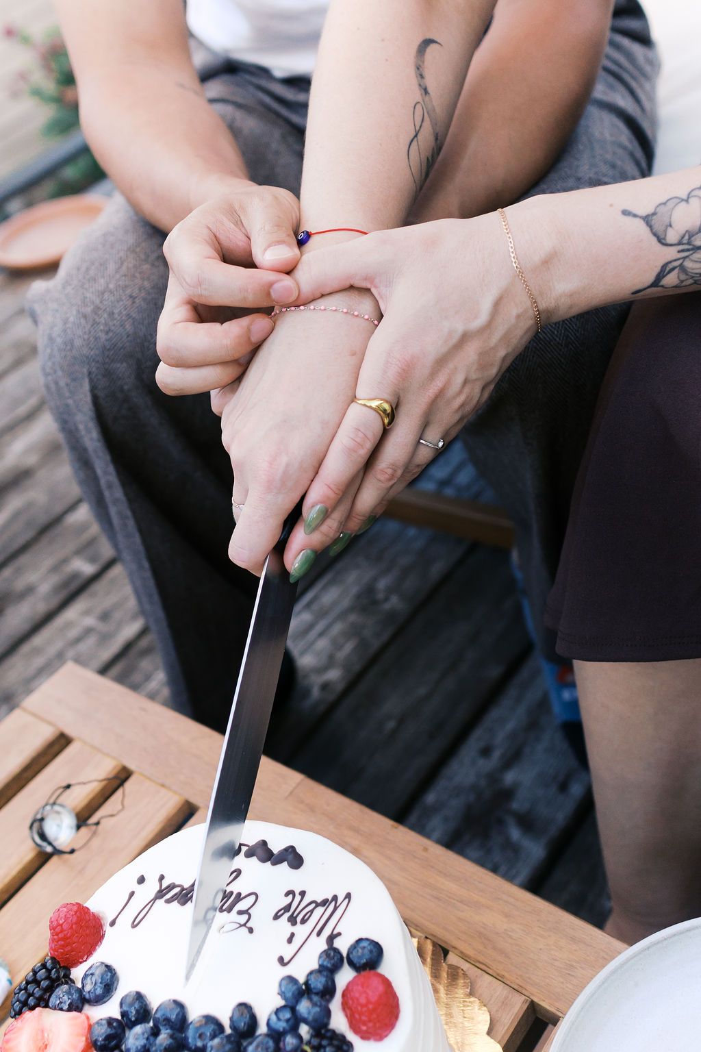 The couple cuts their engagement cake together while holding hands.